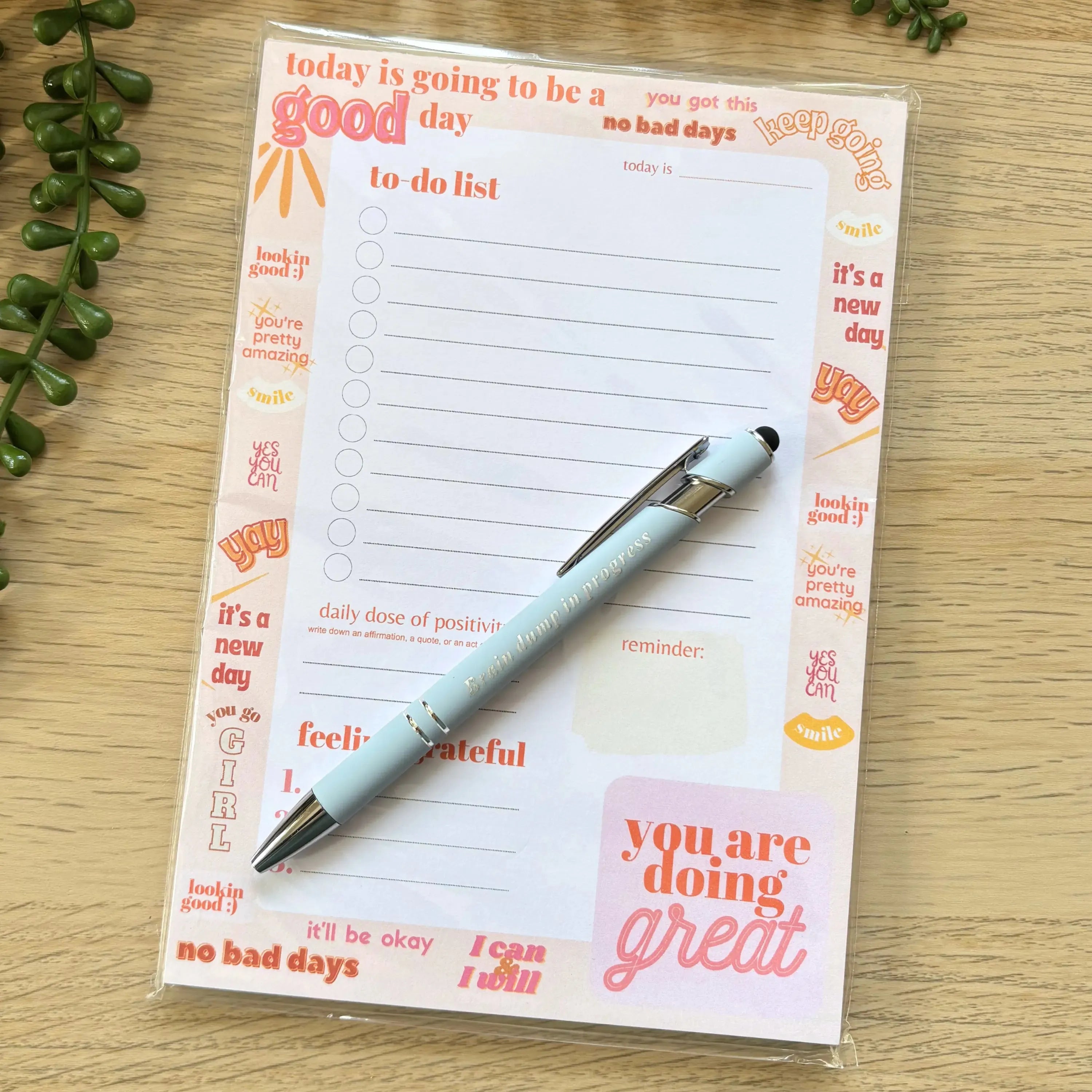 Notepad with motivational quotes and lined to-do list, beige background with orange and red accents.