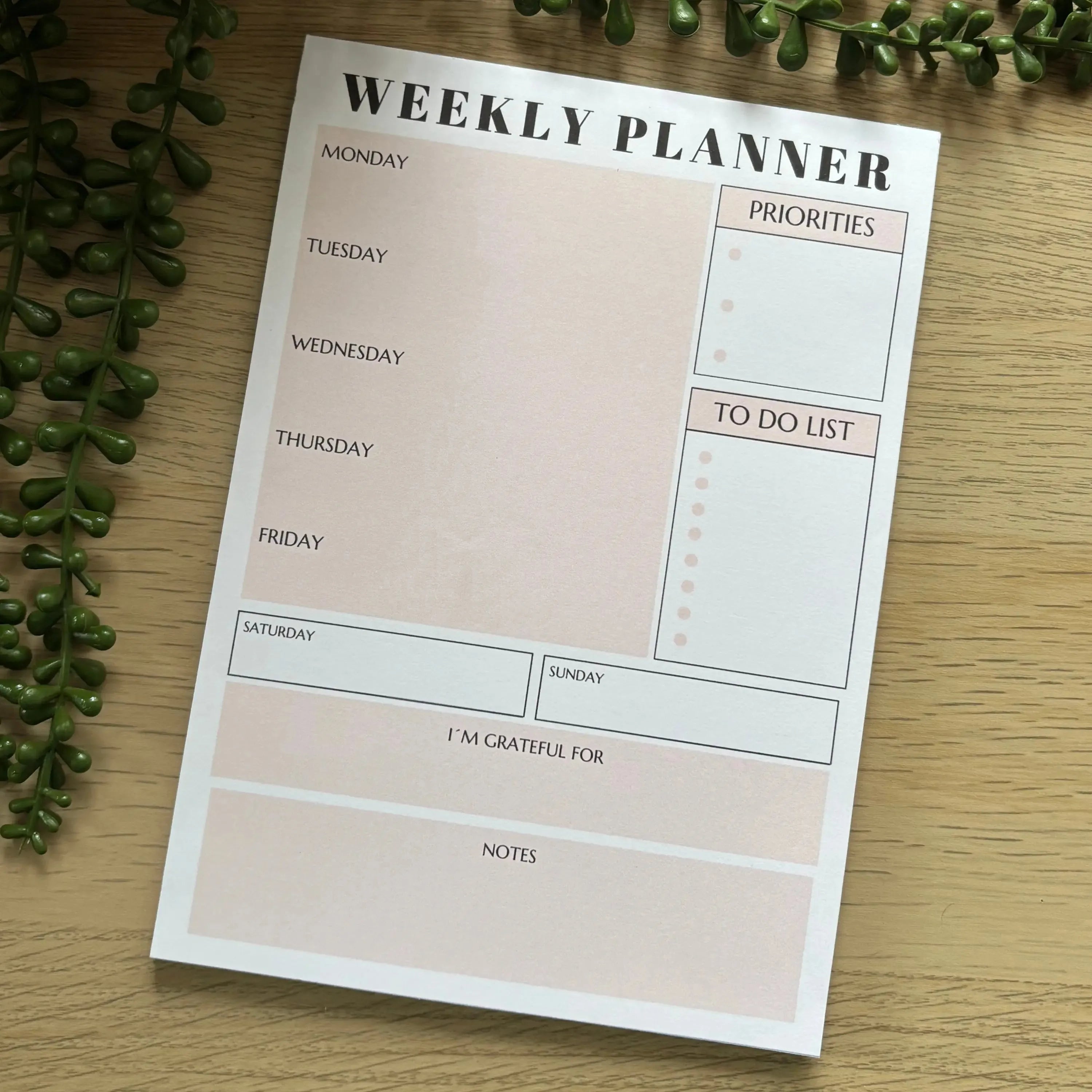 Soft pink weekly planner notepad with days, priorities, to-do list, gratitude, and notes sections.
