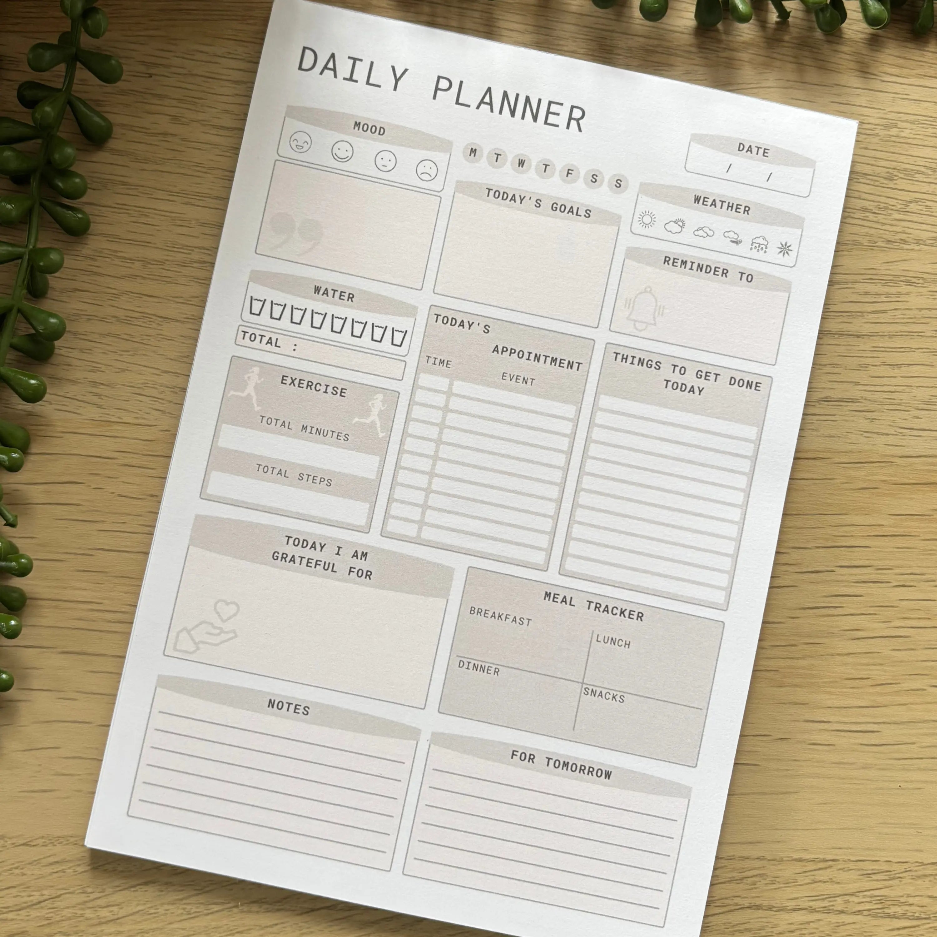 Minimalist daily planner notepad with sections for priorities, schedule, to-do list, meals, notes on wooden surface.