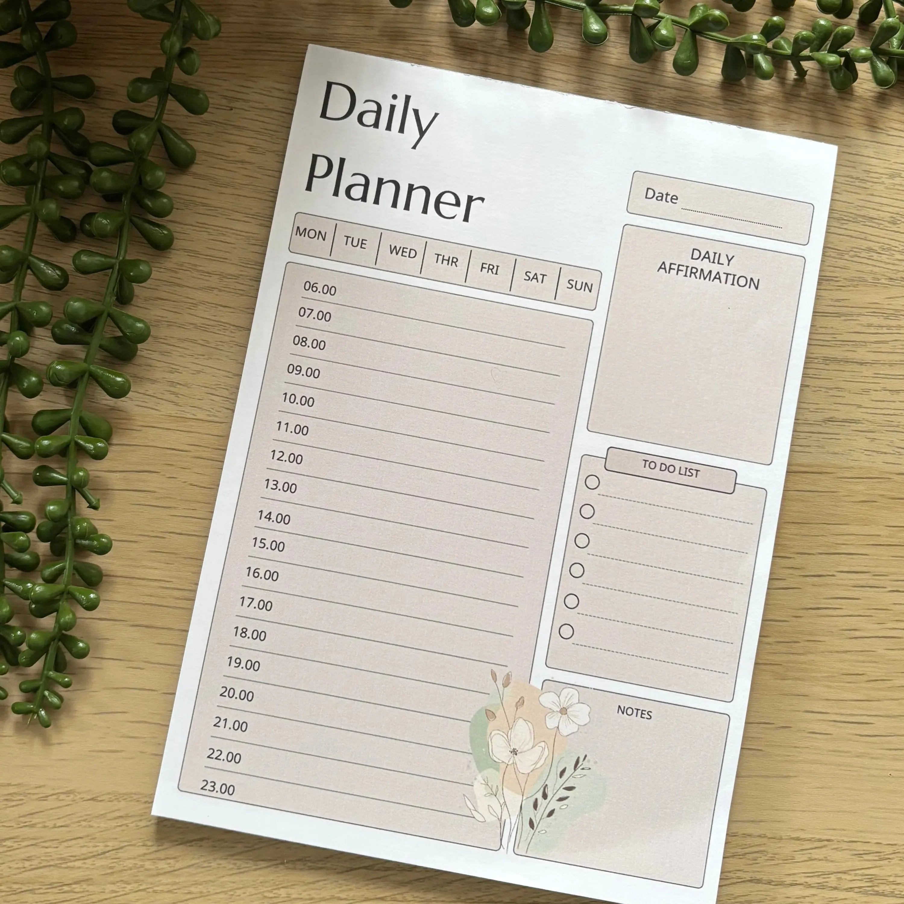 Minimalist daily planner notepad with hourly schedule, to-do list, notes section, and floral design on wooden surface.