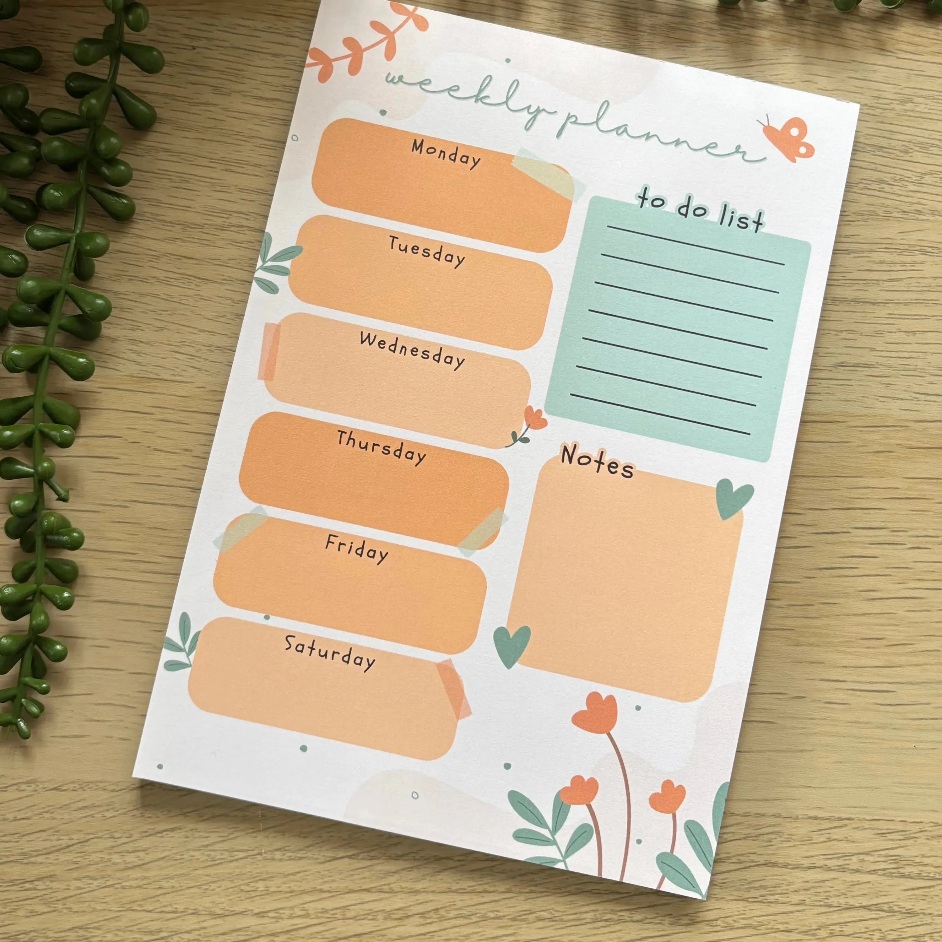 Minimalist weekly planner notepad with orange day blocks, blue to-do list, and notes section on floral background.