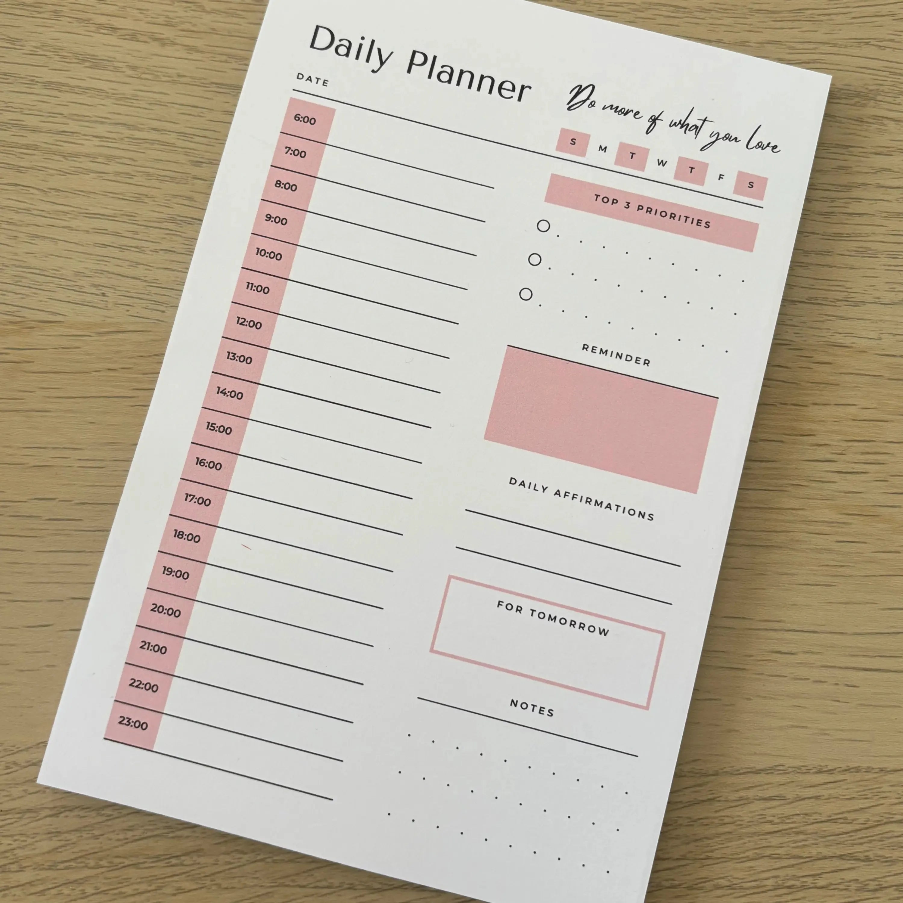 Minimalist daily planner notepad with time slots, to-do list, notes, and highlighted sections on wood surface.