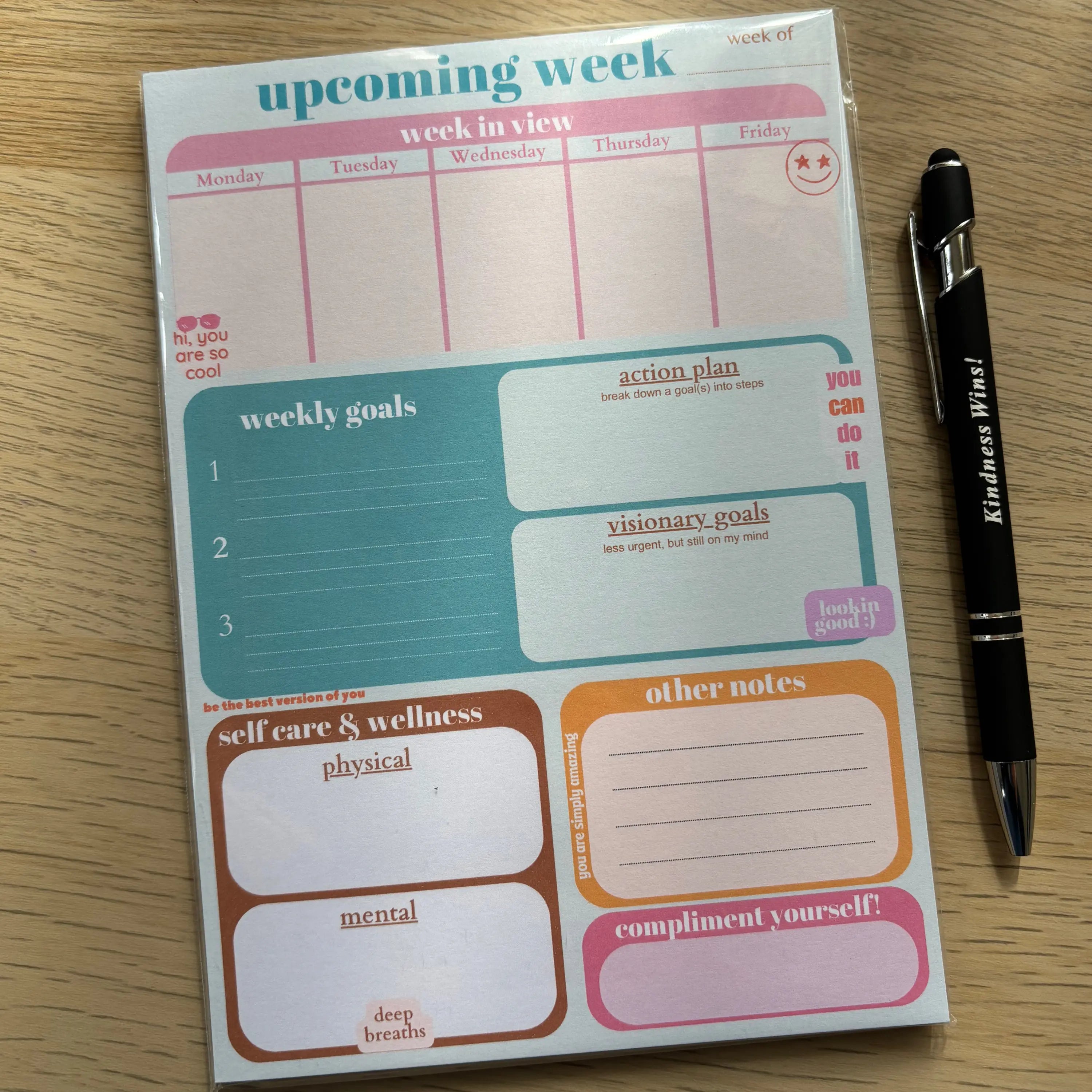 Green weekly planner notepad with sections for goals, notes, self-care, and a black pen on wooden surface.