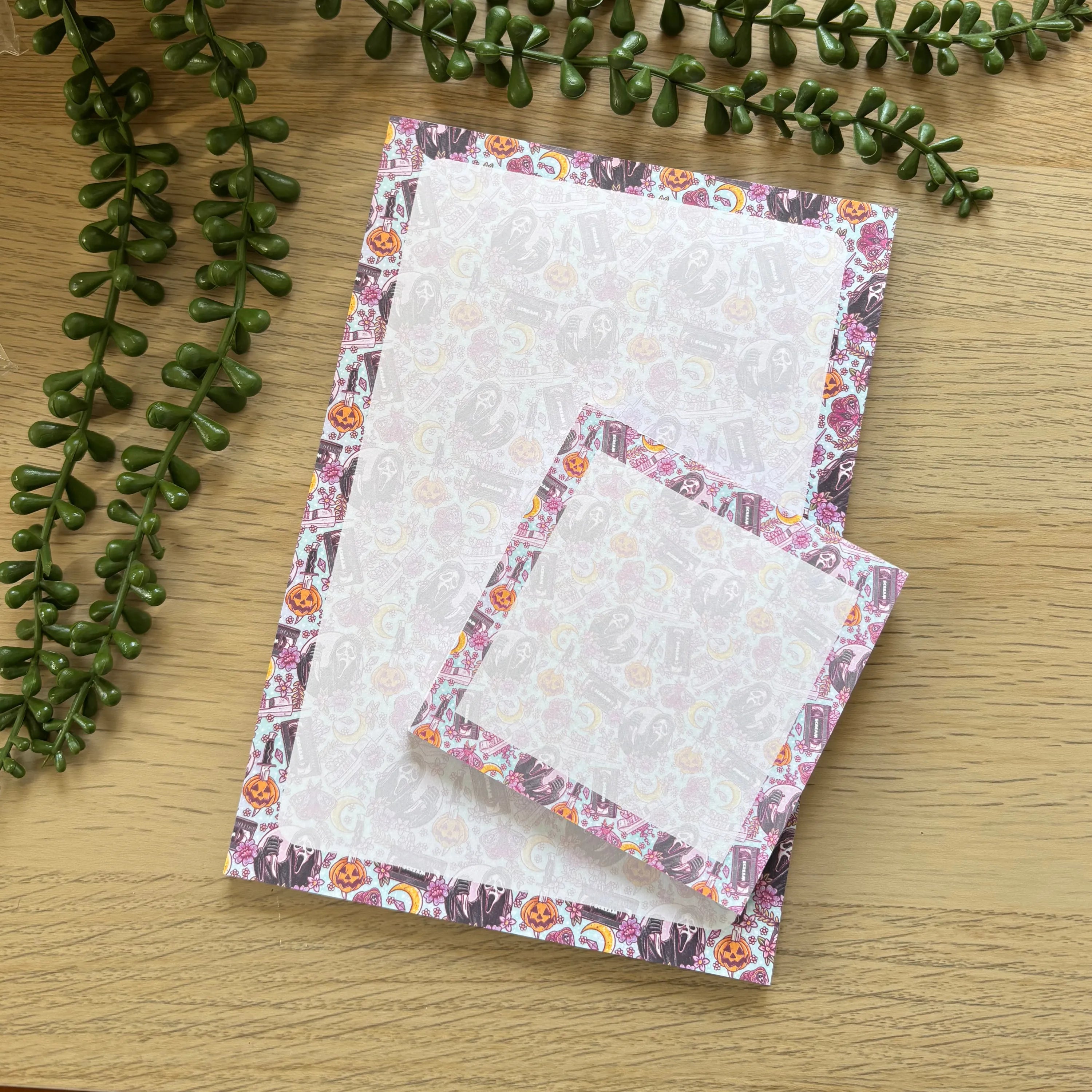 Two pastel notepads with minimalist floral borders on a wooden surface, one large and one mini size.