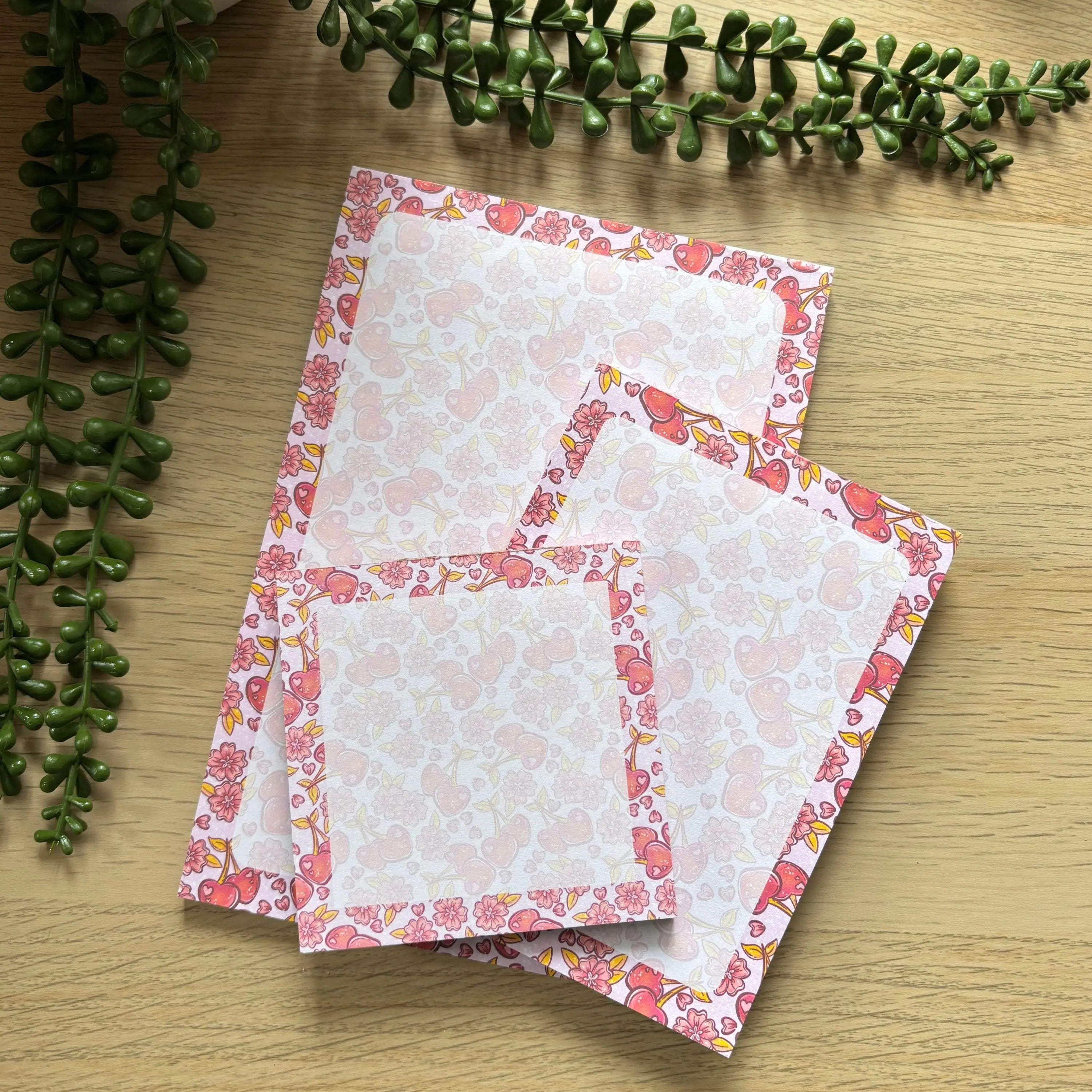 Set of three cherry blossom notepads in mini, small, and large sizes with pink floral borders on a light wood surface.