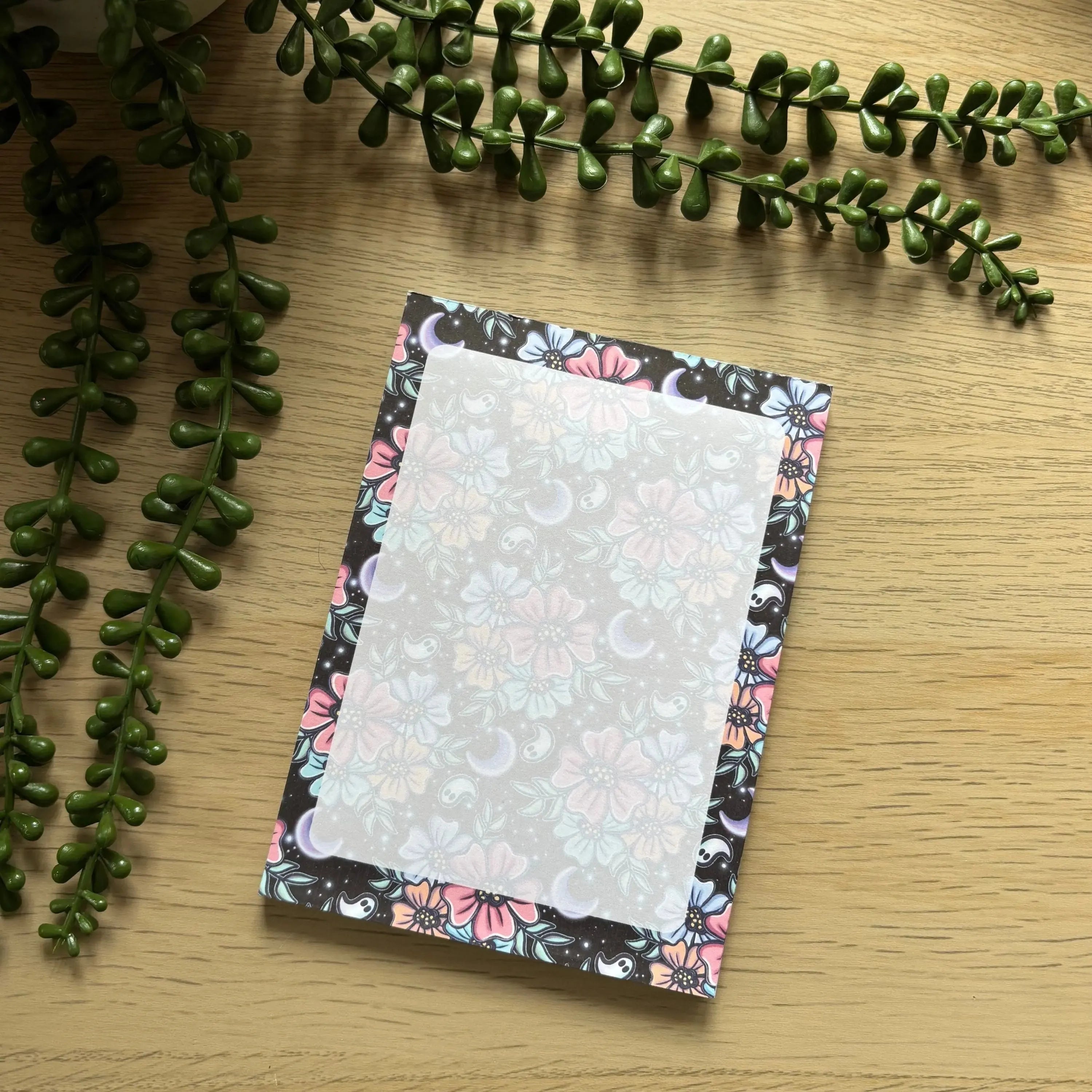 Notepad with a dark floral border featuring pastel pink, blue, and white flowers on light cream writing area.