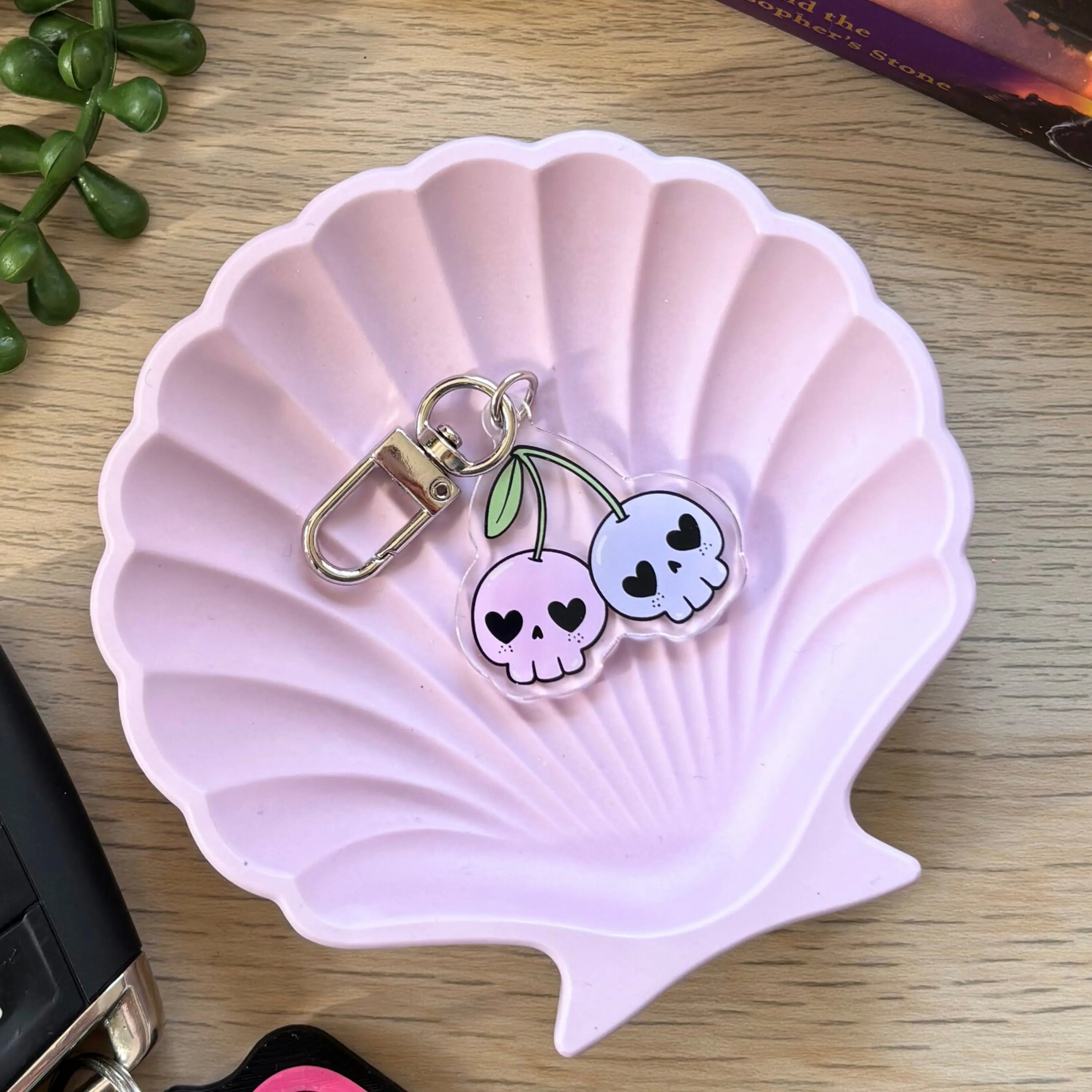 Pink and white cherry skull keyring with green stems on a pink scallop shell dish.