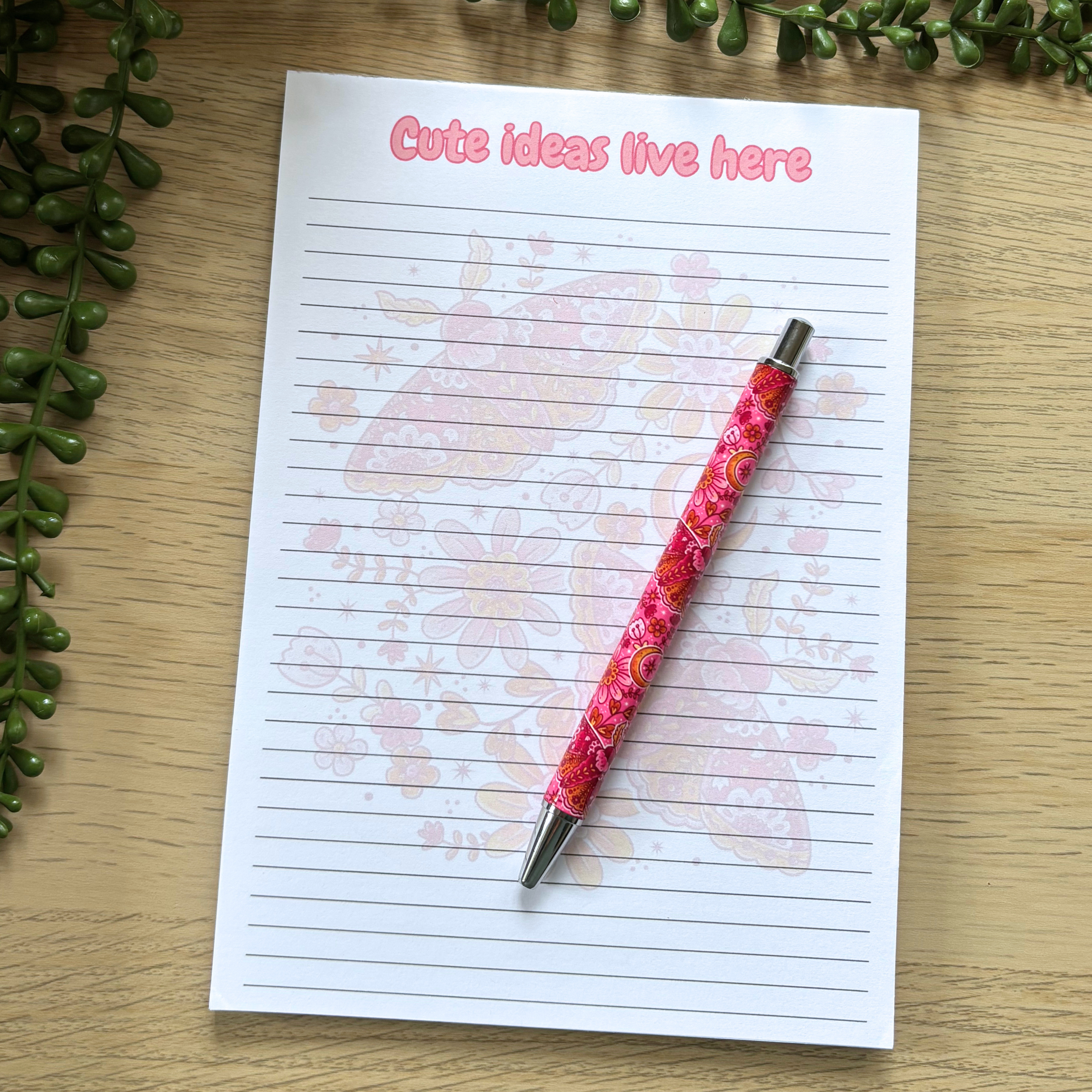 Pink pen with butterfly design on white lined notepad reading "Cute lines live here".