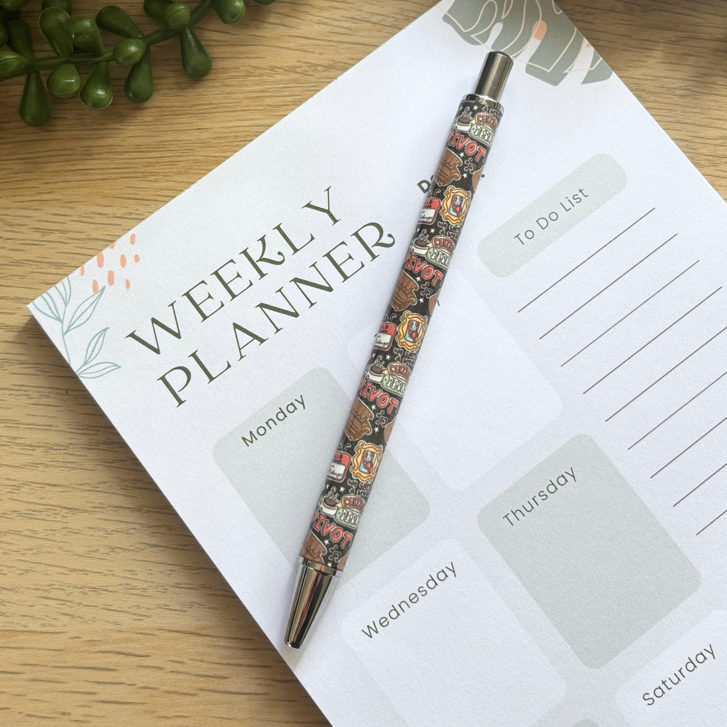 Pen with colorful detailed tattoo-inspired design resting on a weekly planner page with floral accents.