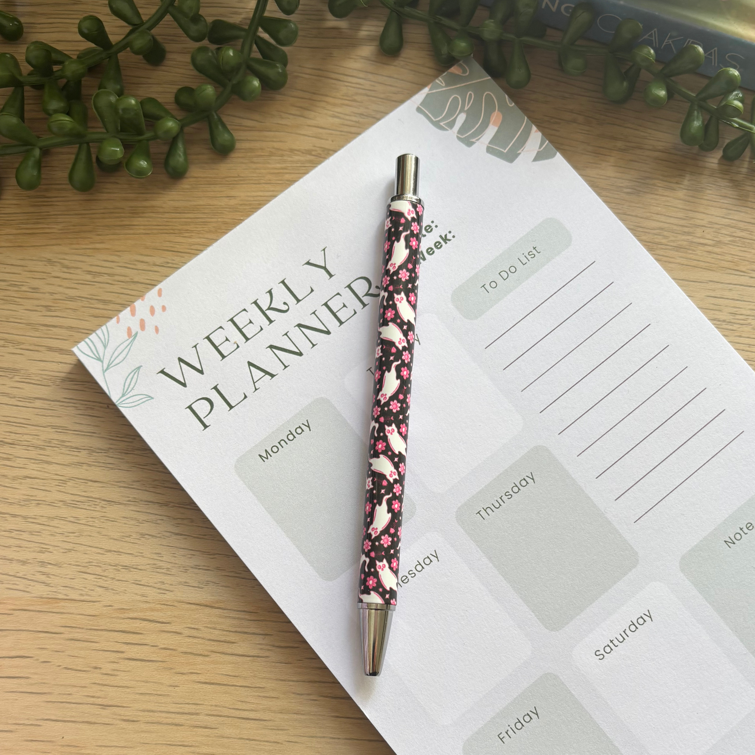 Pink and black Ghost Kitty patterned pen with silver tip resting on weekly planner page.