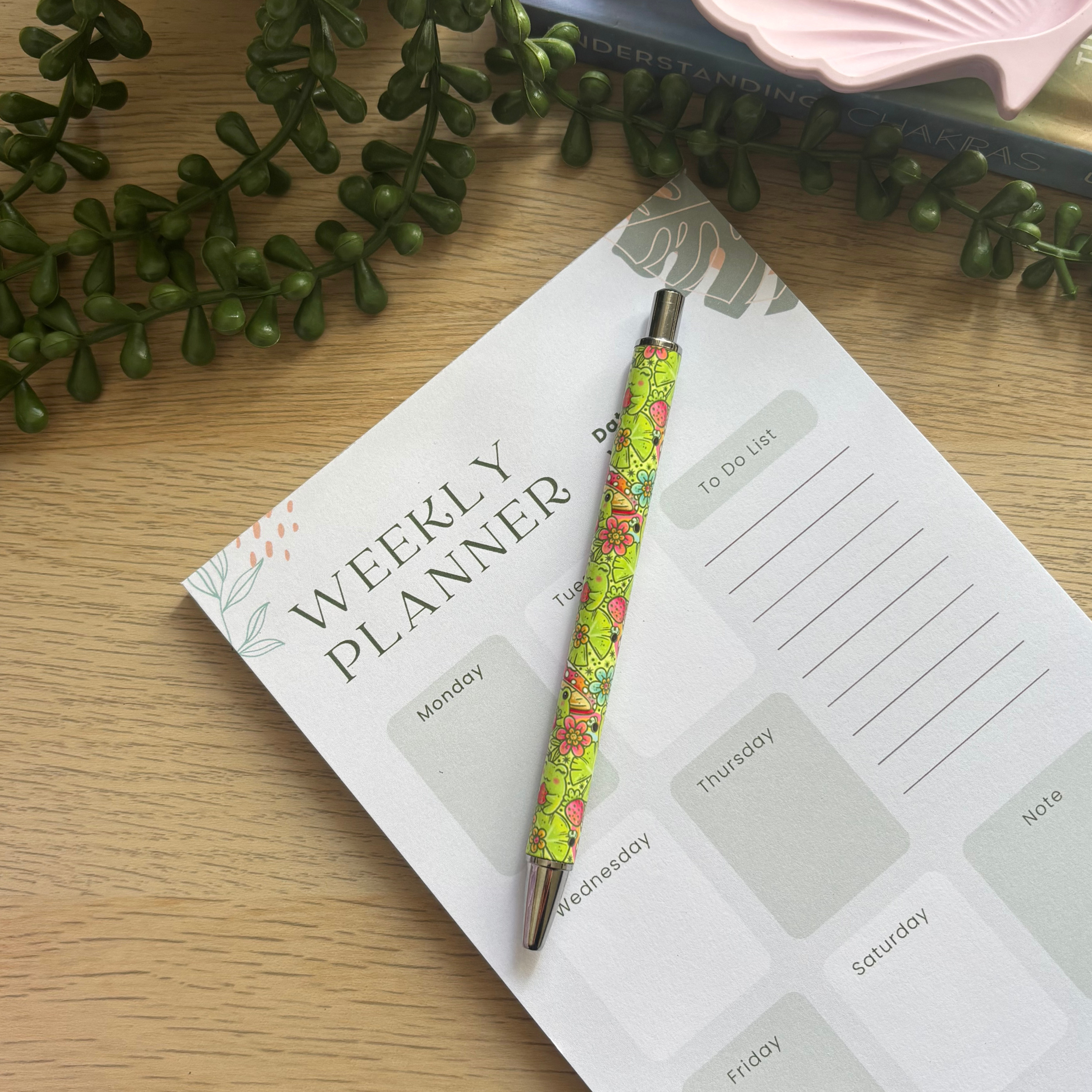Colorful Strawberry Frog pen with pink and green floral pattern resting on a weekly planner page.