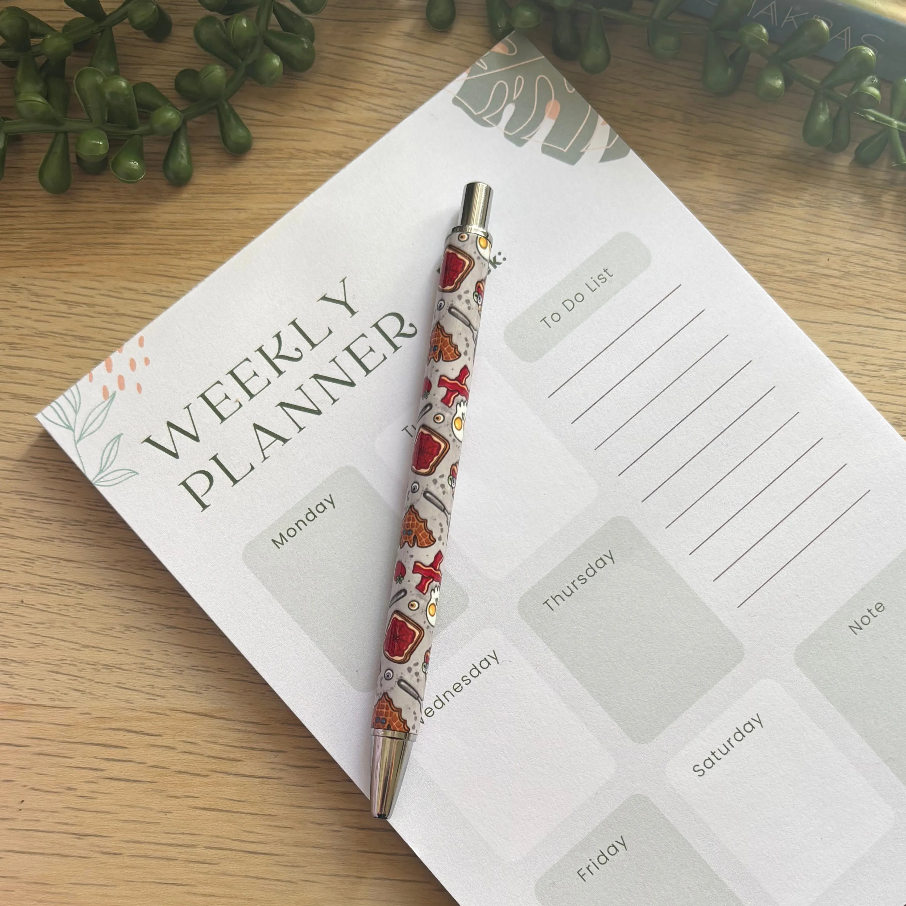 White pen with red and black spooky tattoo-style illustrations placed on a weekly planner page on a wooden desk.