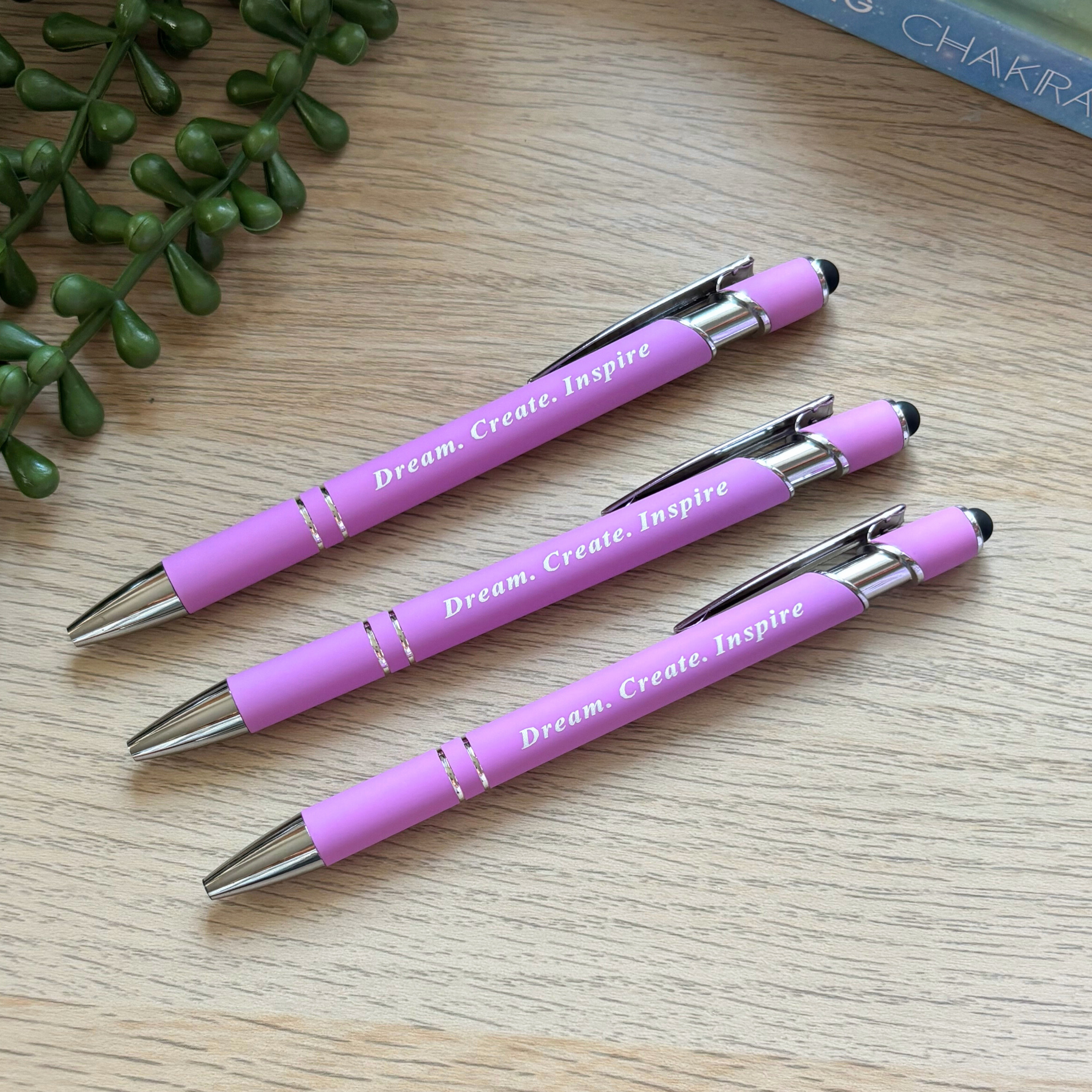 Set of three pink pens with silver tips and clips, each engraved with "Dream. Create. Inspire" in white text.