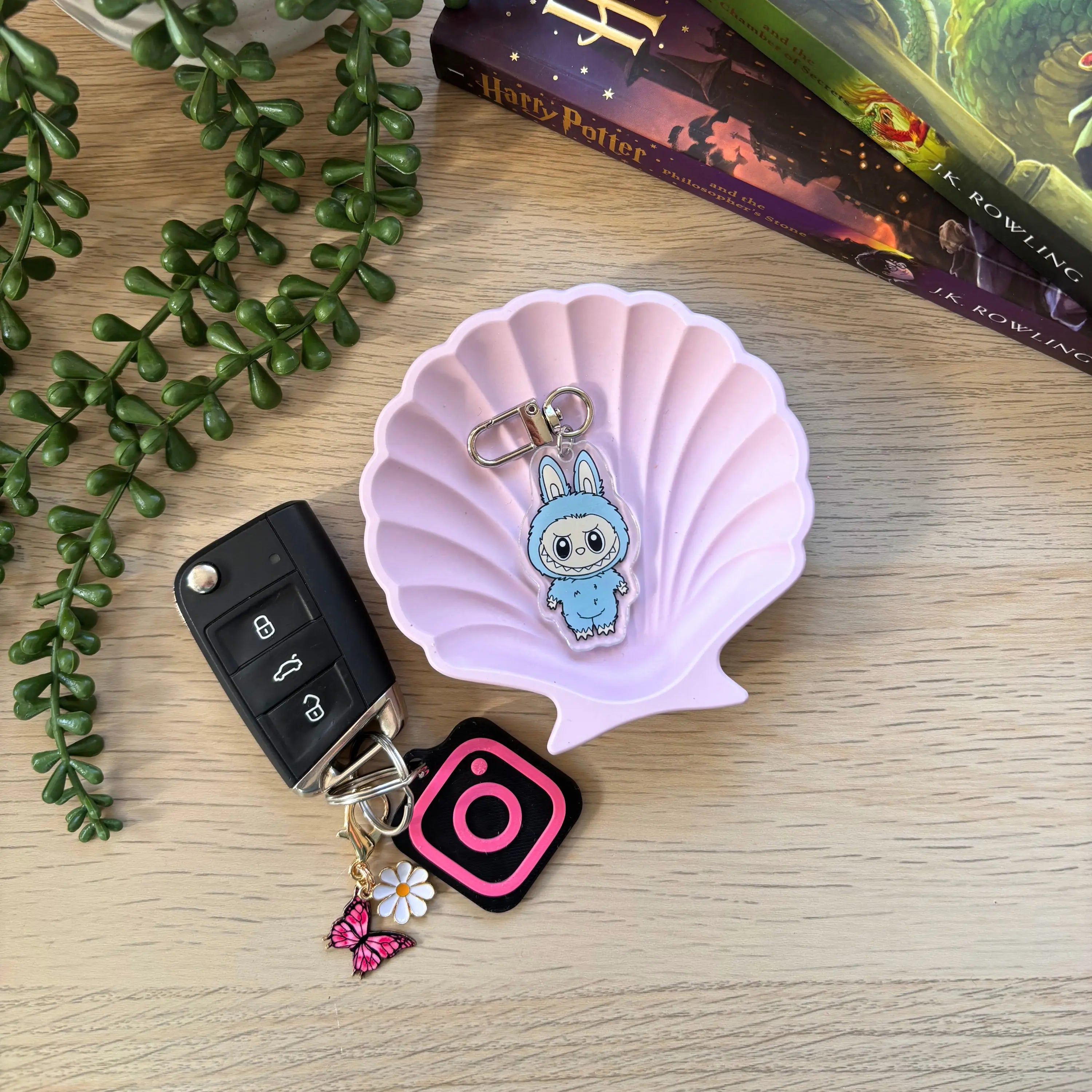 Blue Labubu character keyring with shell-shaped purple tray and attached to black car key fob with pink Instagram charm and.