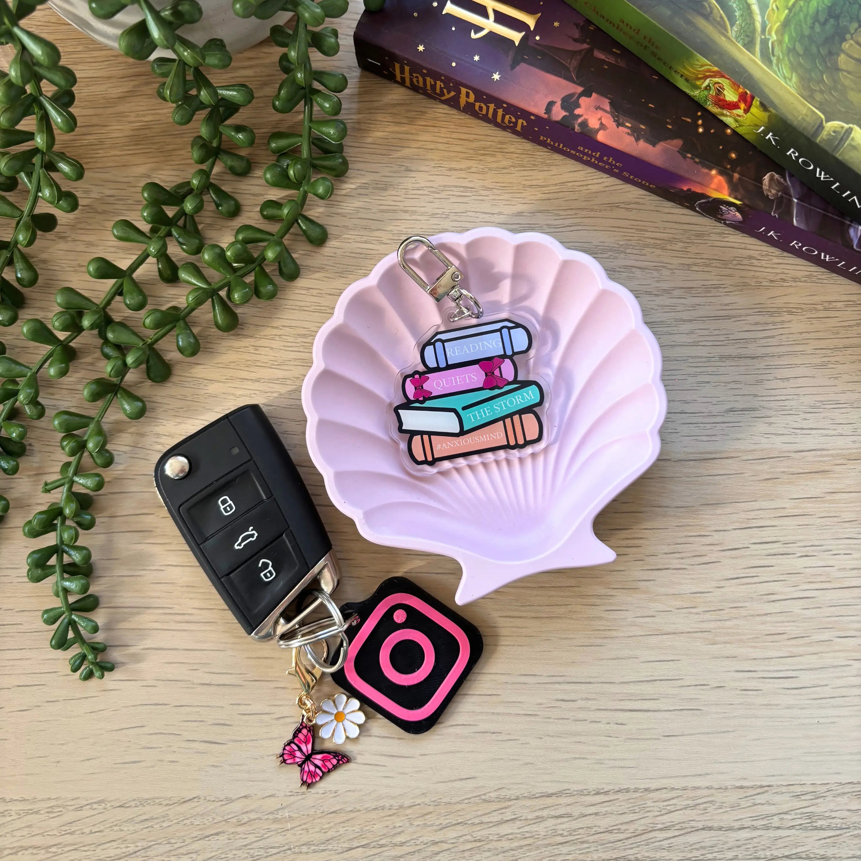 Keyring with colorful stack of books charm and two additional charms, including Instagram logo, displayed on a pink shell.