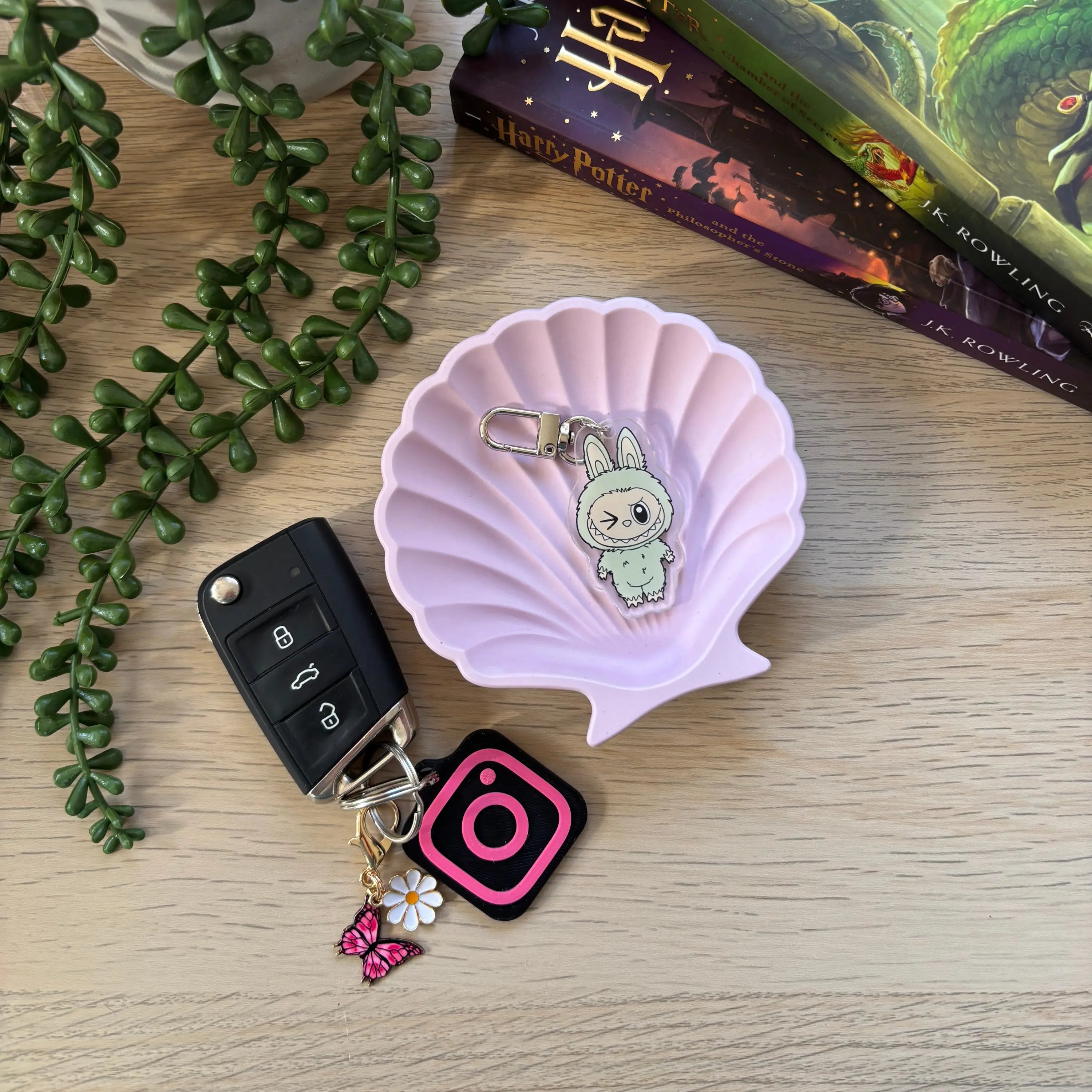 Cute green character keyring with large eyes, attached to a silver keychain ring and pink phone charm.