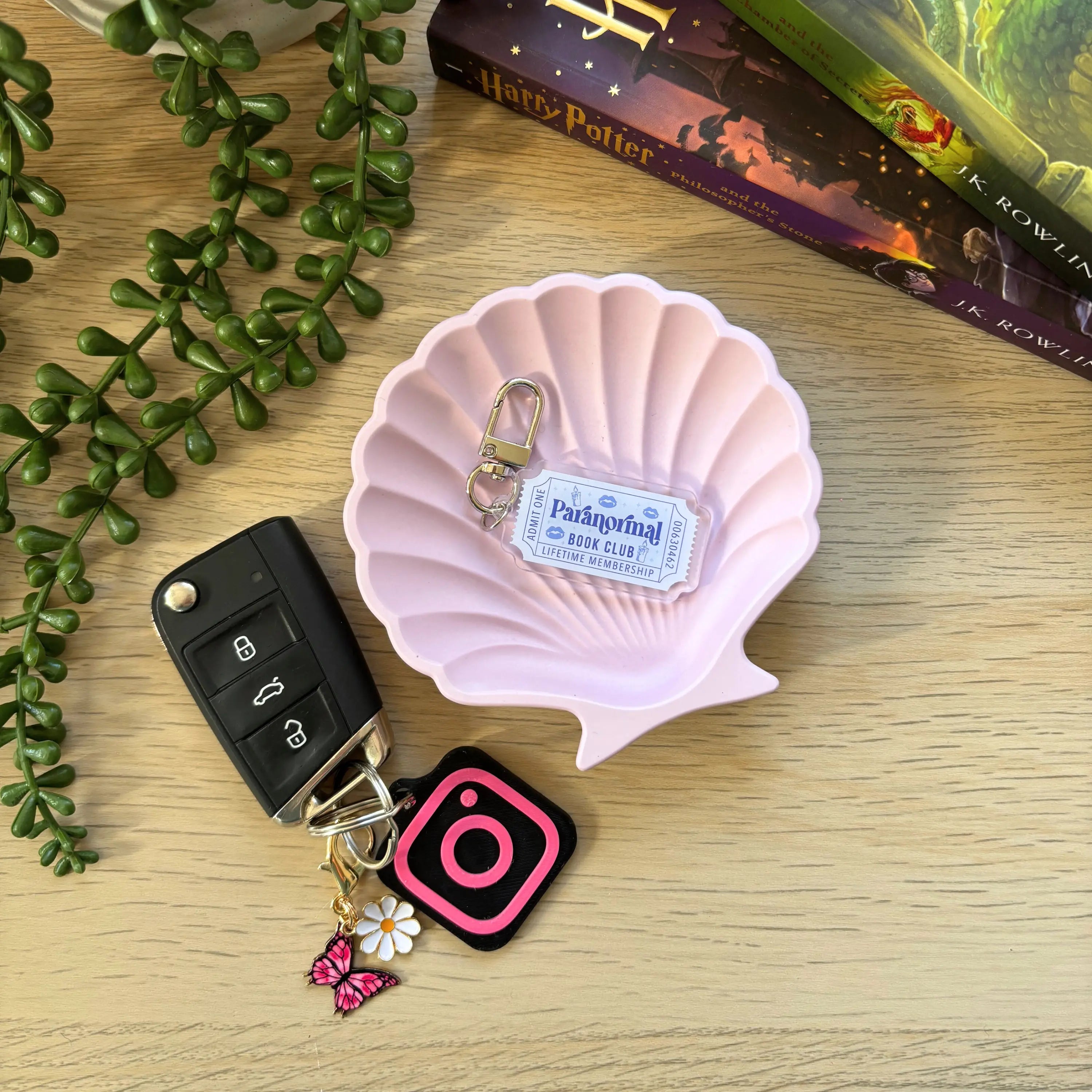 Clear acrylic keyring shaped like a ticket with "Paranormal Bookish Ticket" text on a silver chain, displayed on a pink.