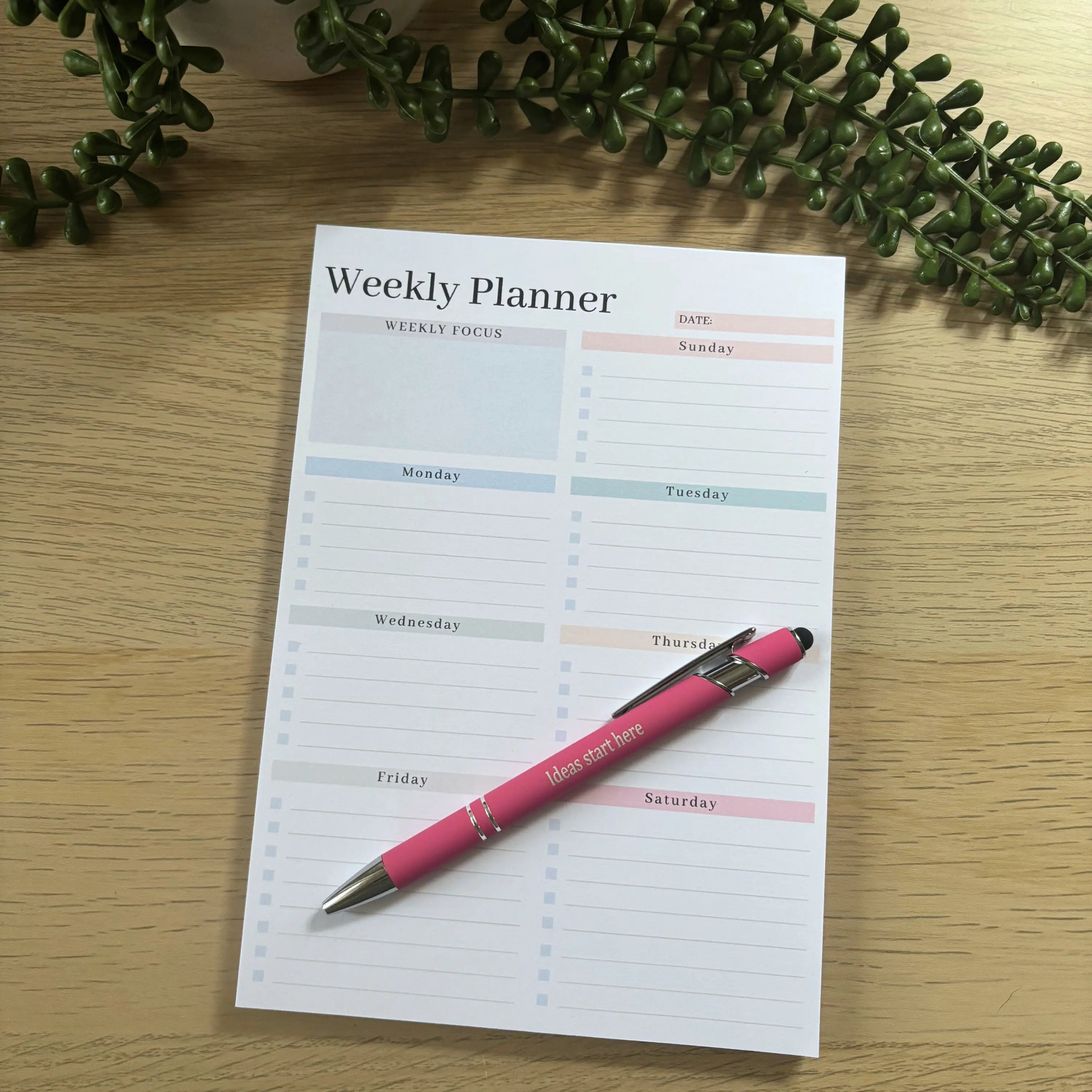 Minimalist weekly planner notepad with sections for days of the week on wooden surface with pink pen.