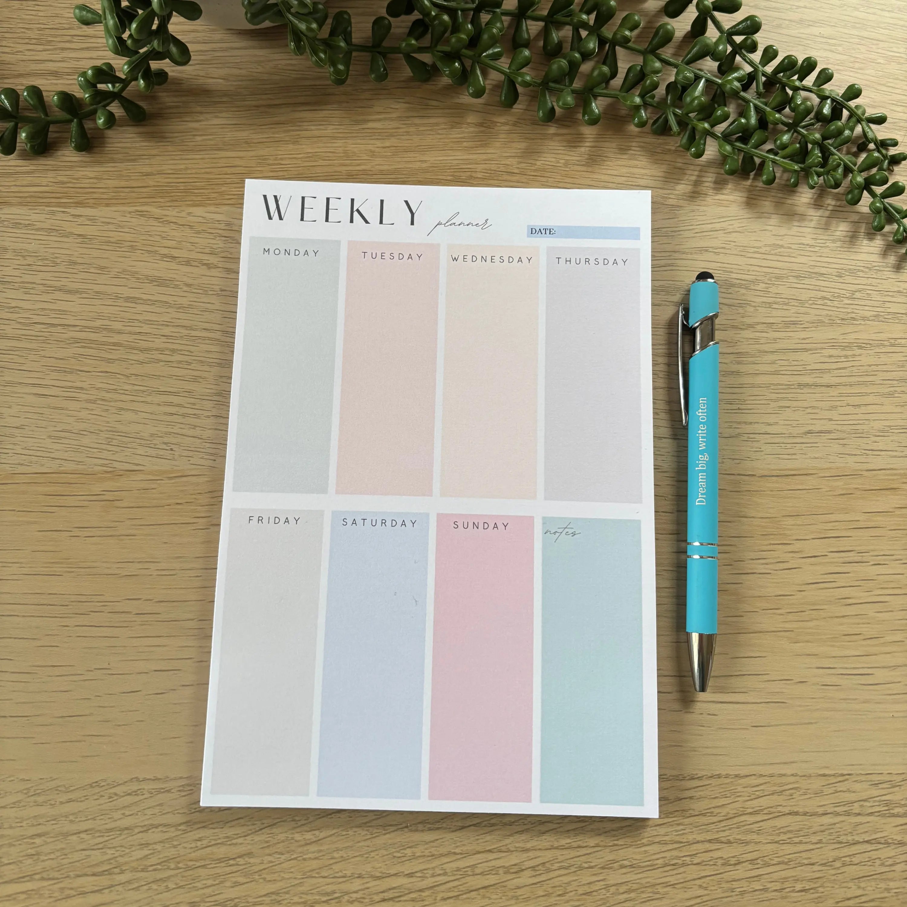 Weekly block planner notepad with pastel-colored daily sections and space for notes on wood surface.