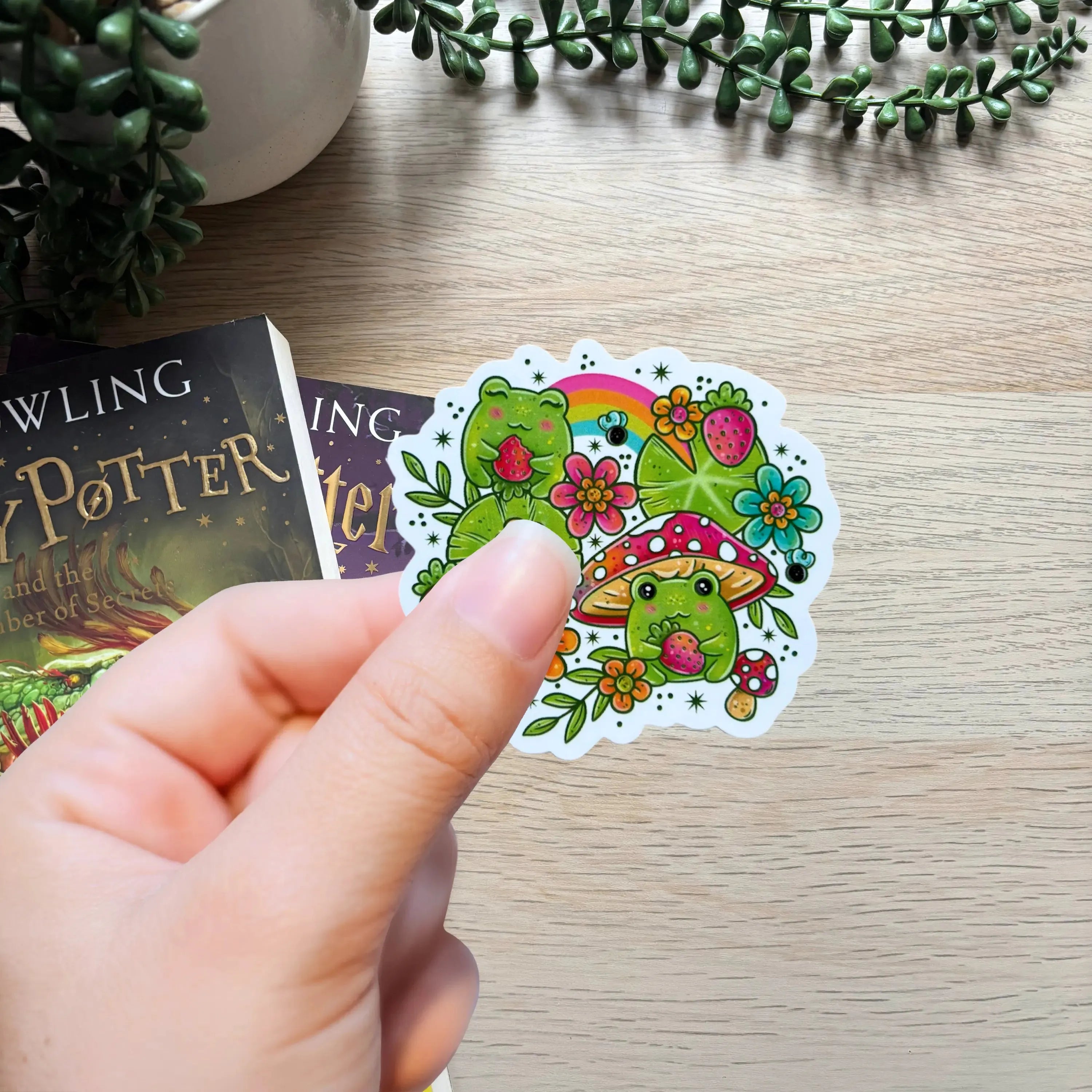 Colorful sticker of a cute frog wearing a strawberry hat with flowers and leaves.