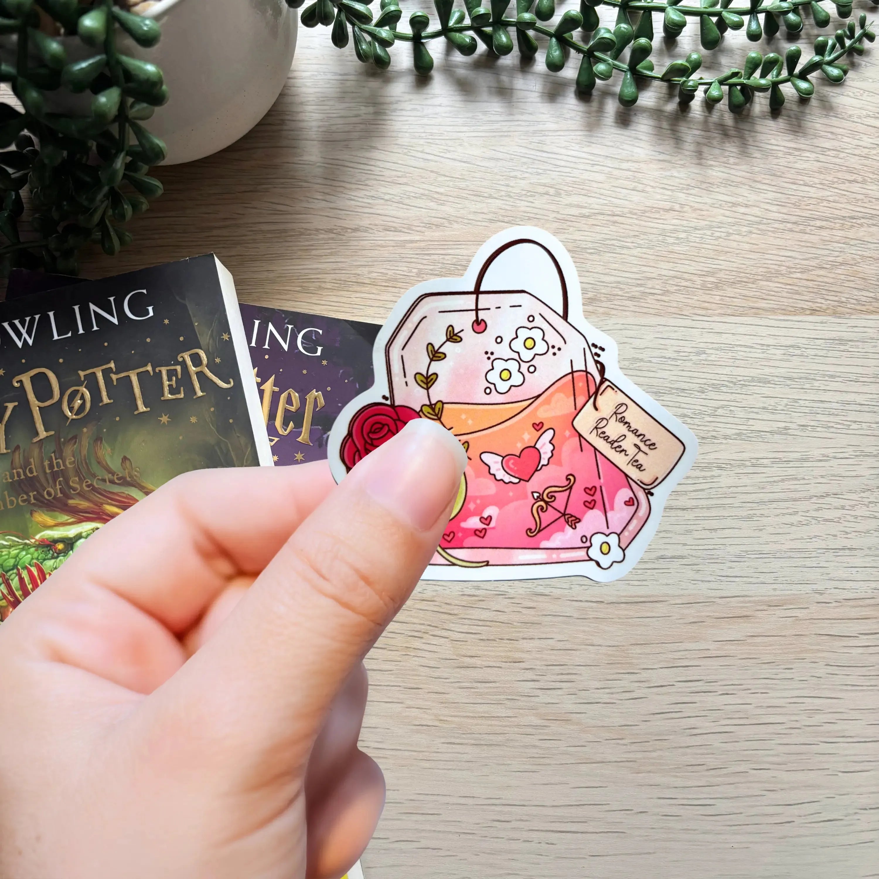 Hand holding Romance Reader sticker featuring pink teacup, heart, rose, and love note design.