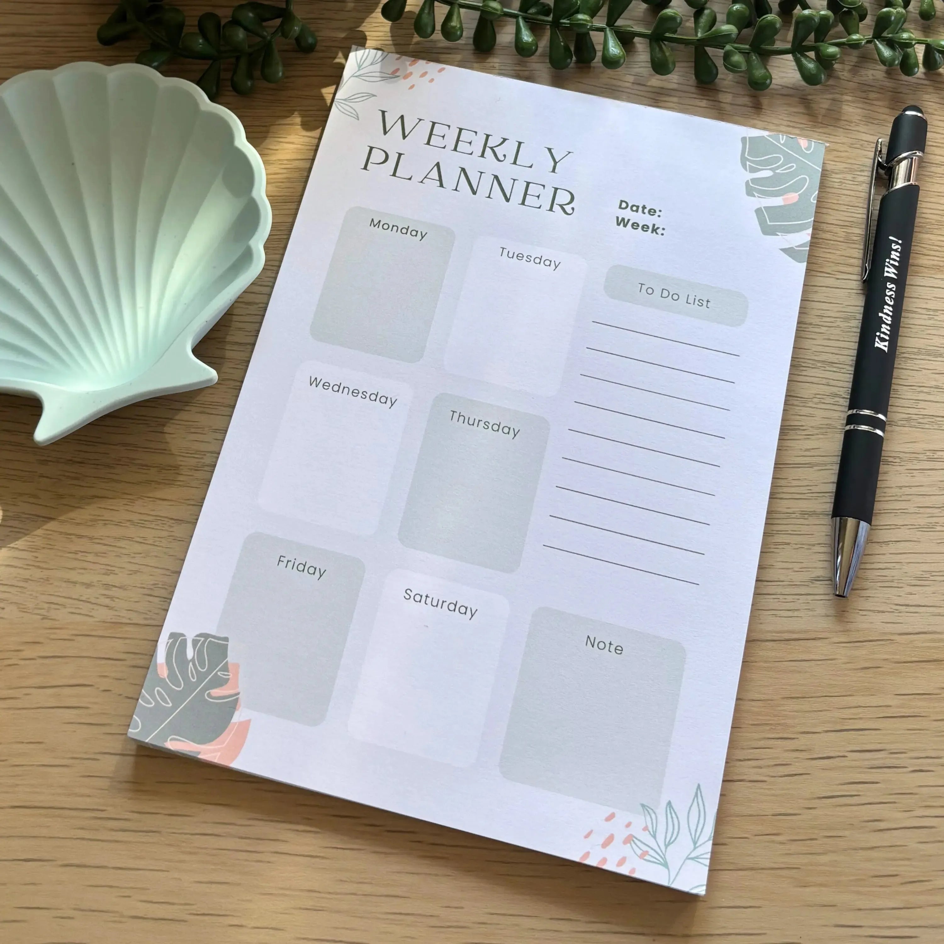 Minimalist weekly planner notepad with botanical illustrations and lined to-do list section on wooden desk.