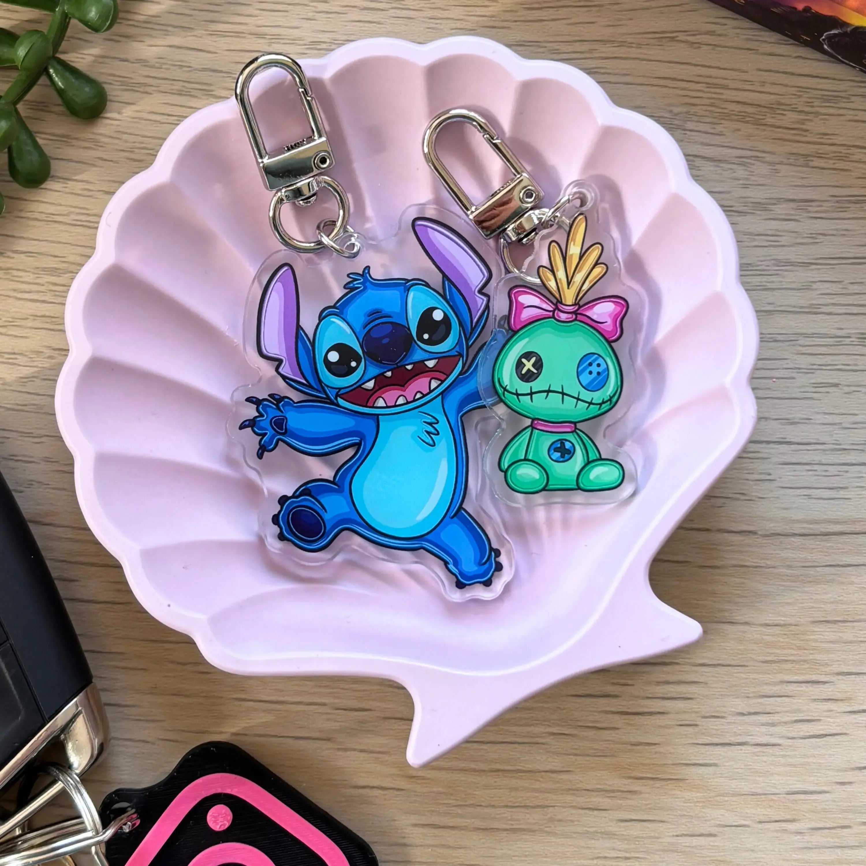 Blue alien character keyring with big eyes and open arms, next to a small green alien with pink bow and stitched mouth, both .