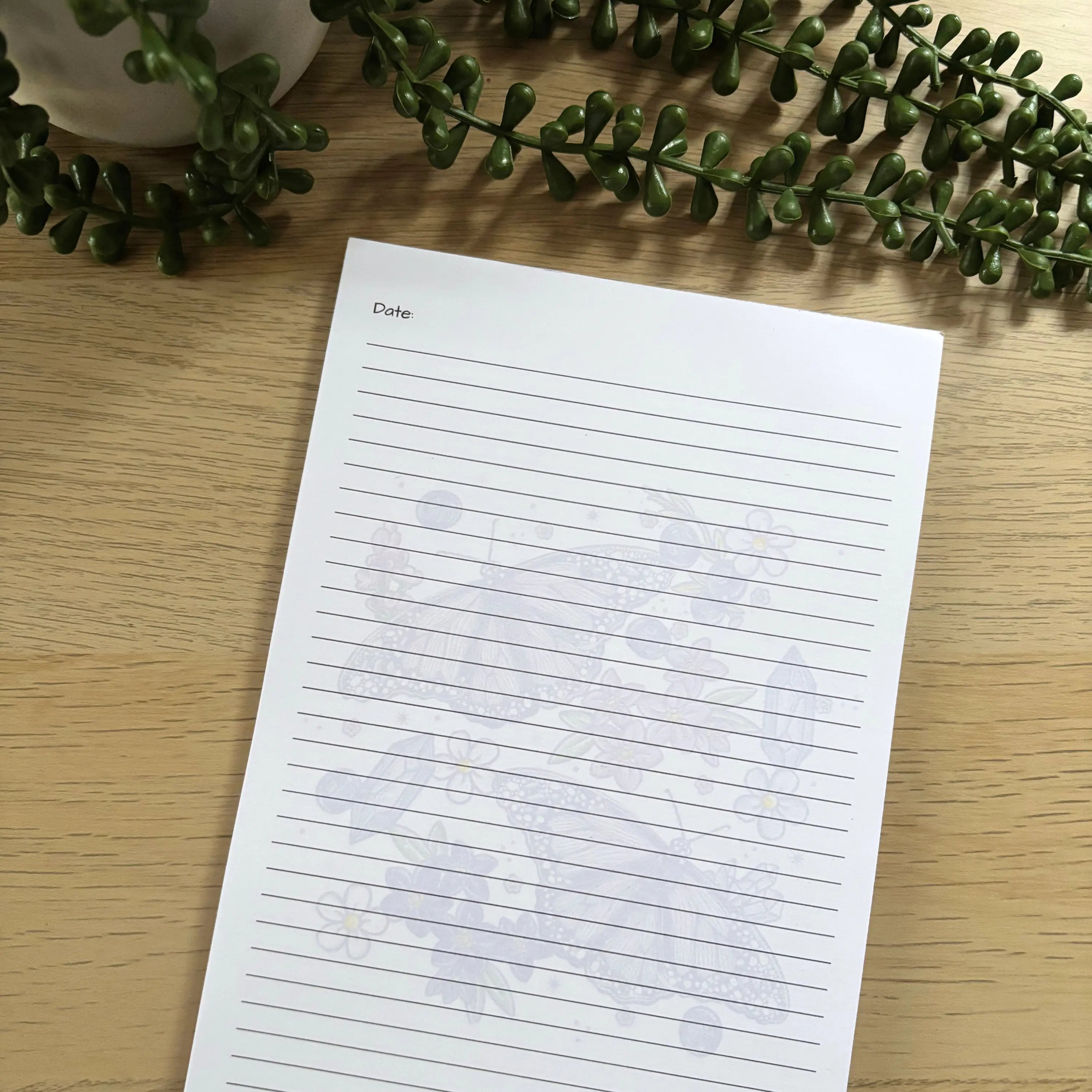 A5 notepad with faint purple butterfly design behind blue horizontal lines on white paper.