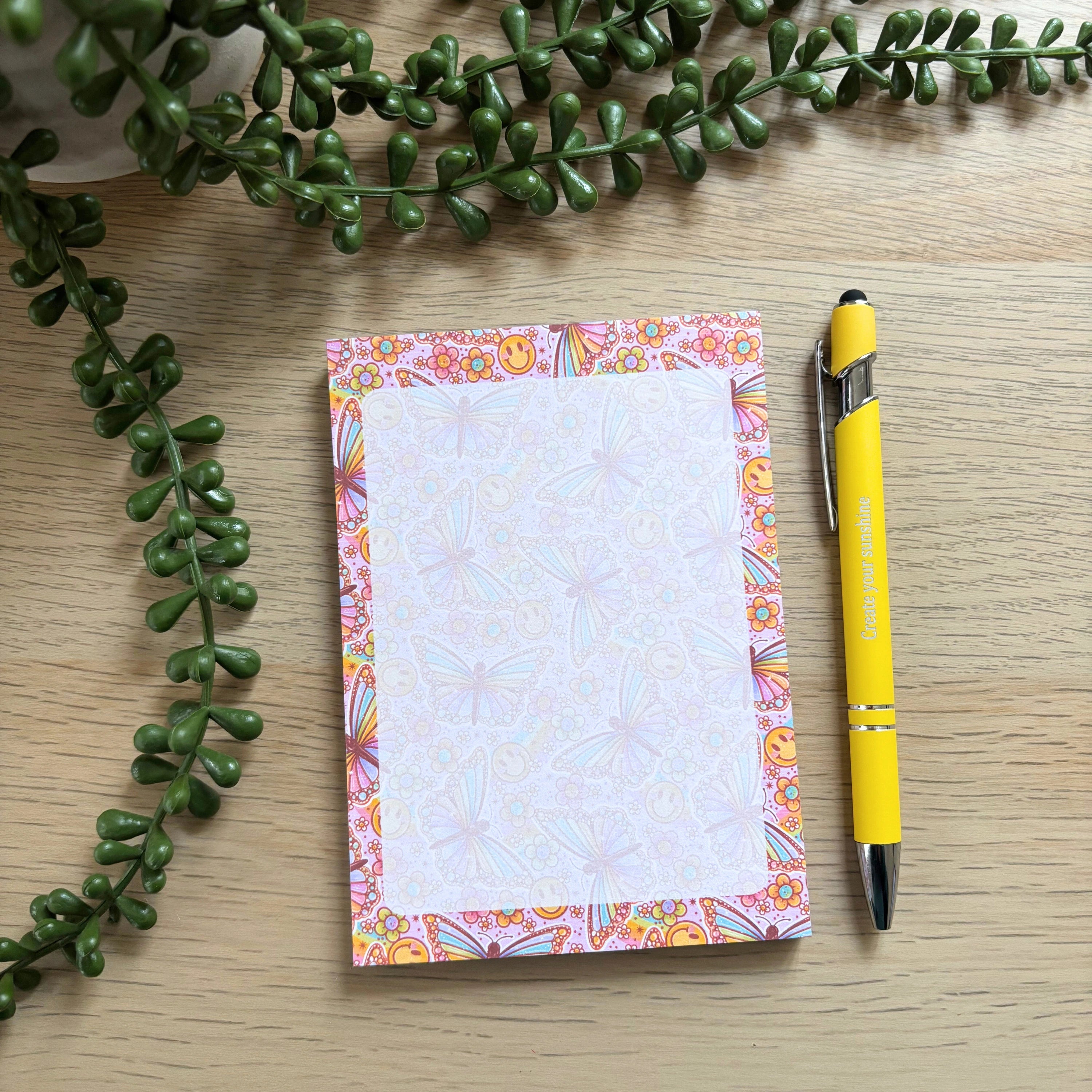 Notebook with colorful border and yellow pen on a wooden surface with green leaves.