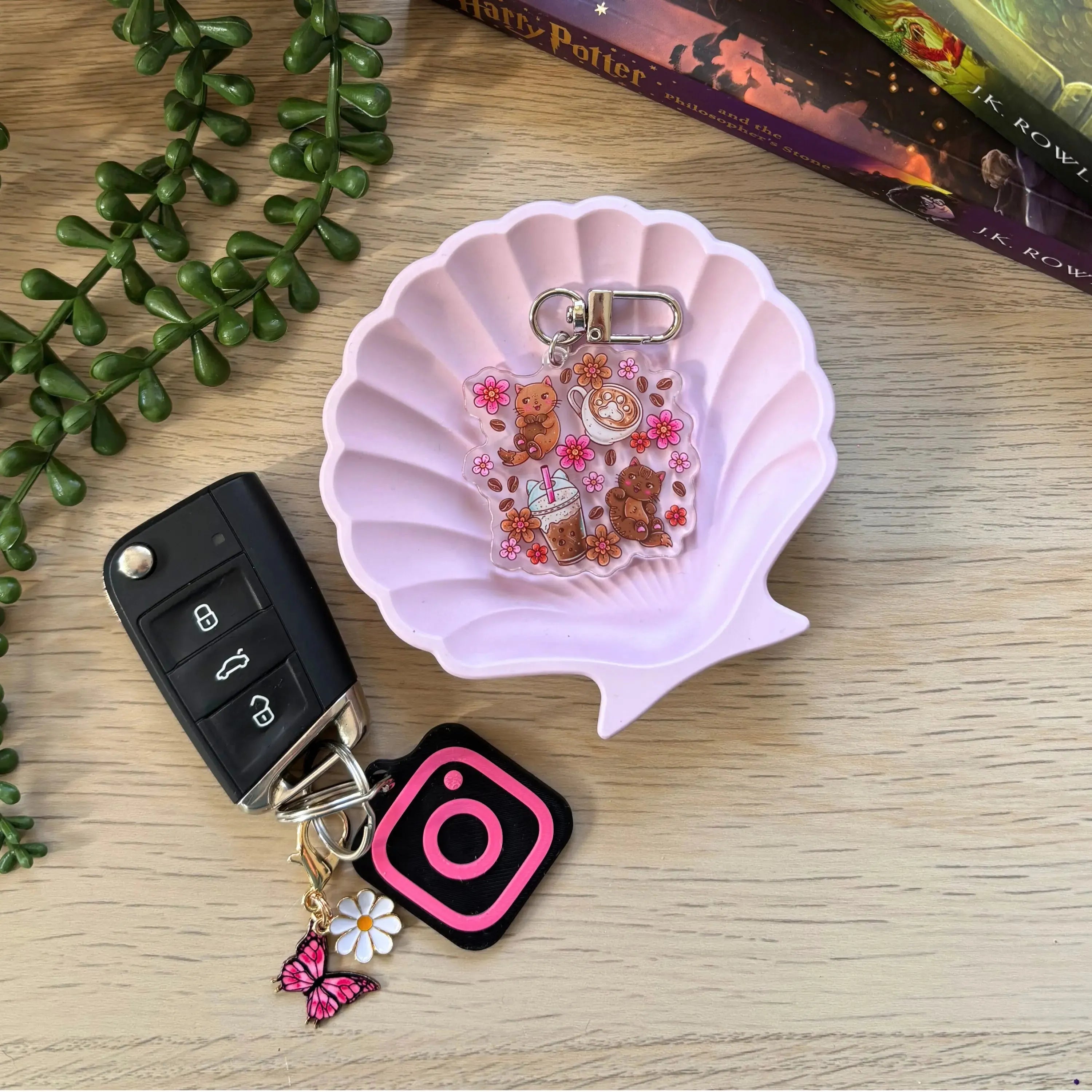 Clear acrylic keyring featuring three illustrated cats with flowers and books on a ring clasp in a pink shell dish.
