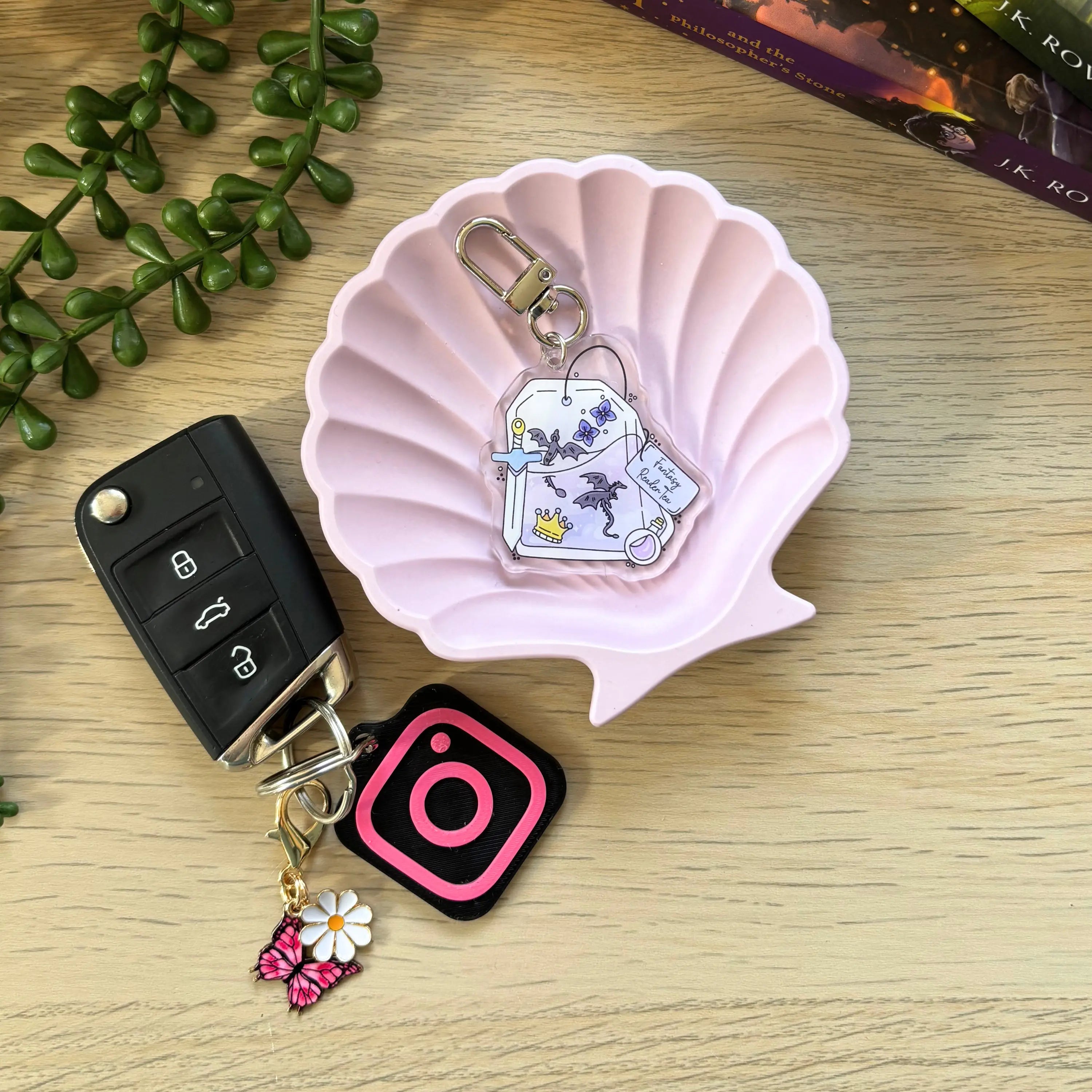 Clear acrylic keyring shaped like a teabag with stars and moons inside, on a pink shell dish next to a car key with charms.