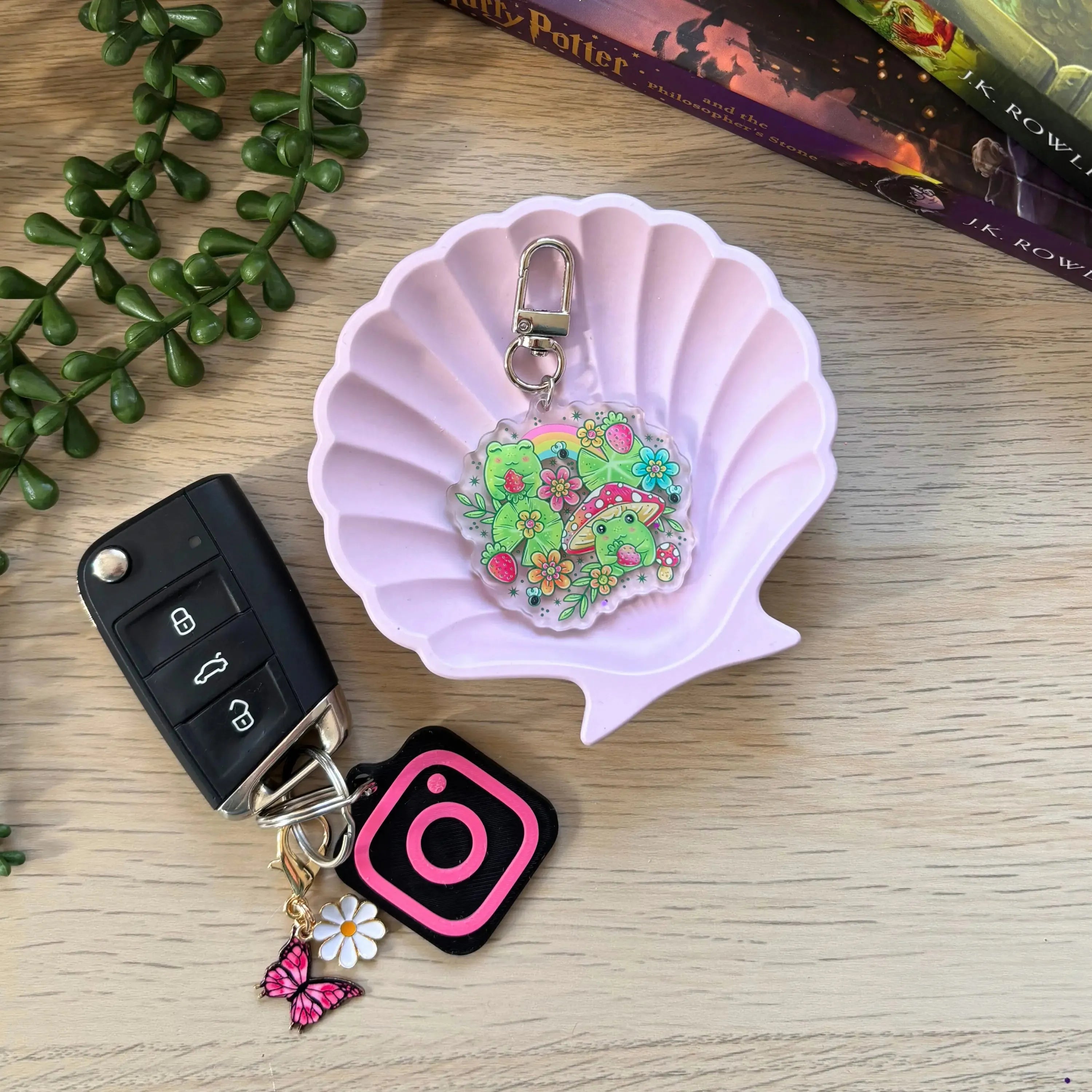 Colorful strawberry frog keyring with floral patterns and silver clasp on pink shell dish.