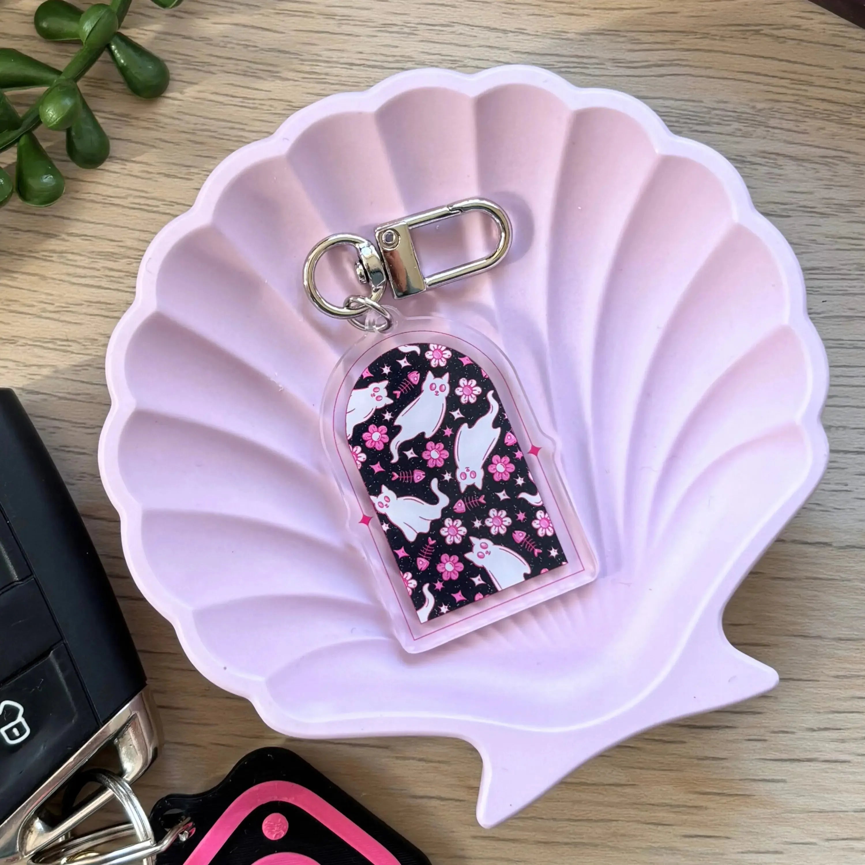 Clear acrylic keyring with a white ghost cat and pink flowers inside a rounded arch shape.