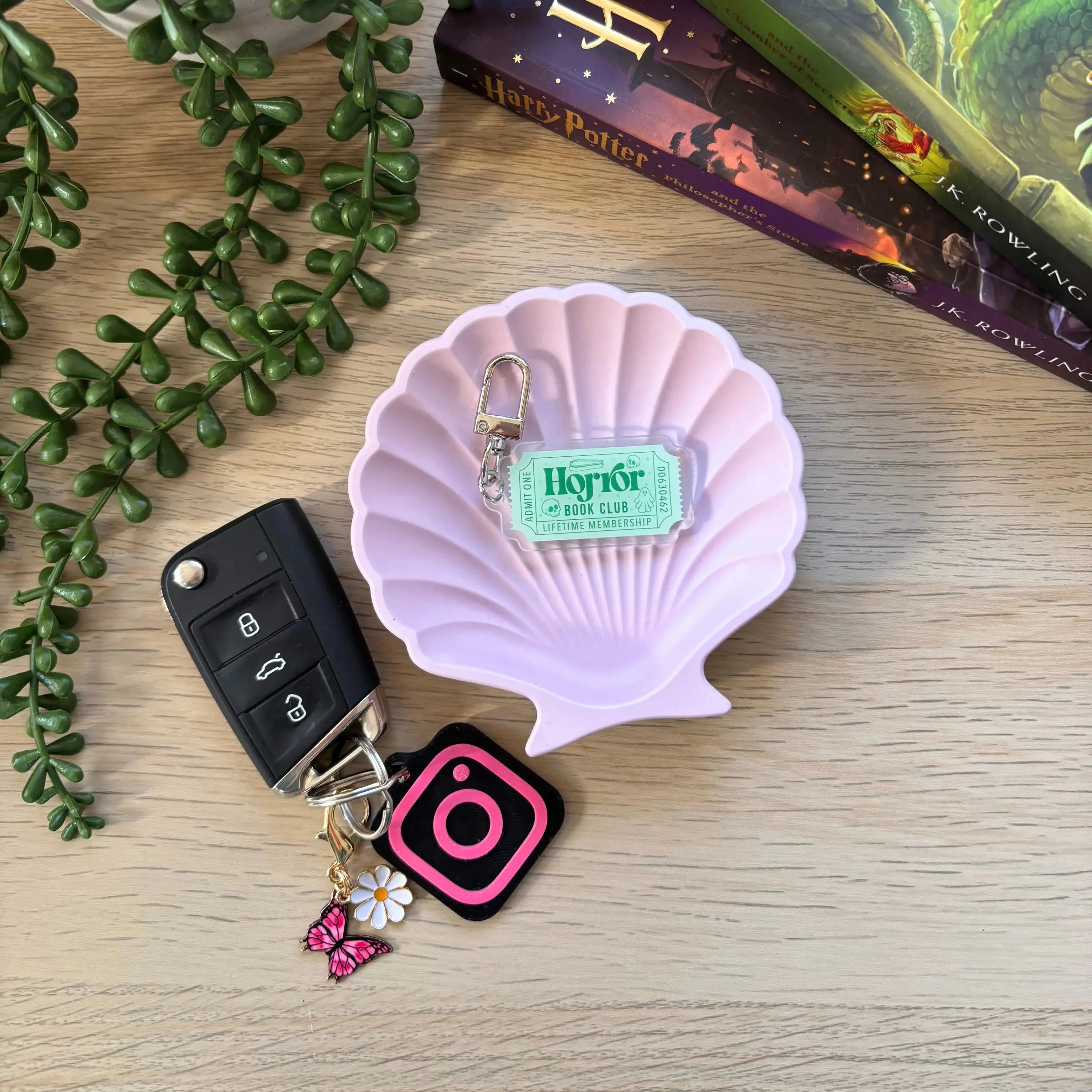 Horror Bookclub keyring with mint green tag attached to pink shell-shaped dish on wooden surface near car keys and books.