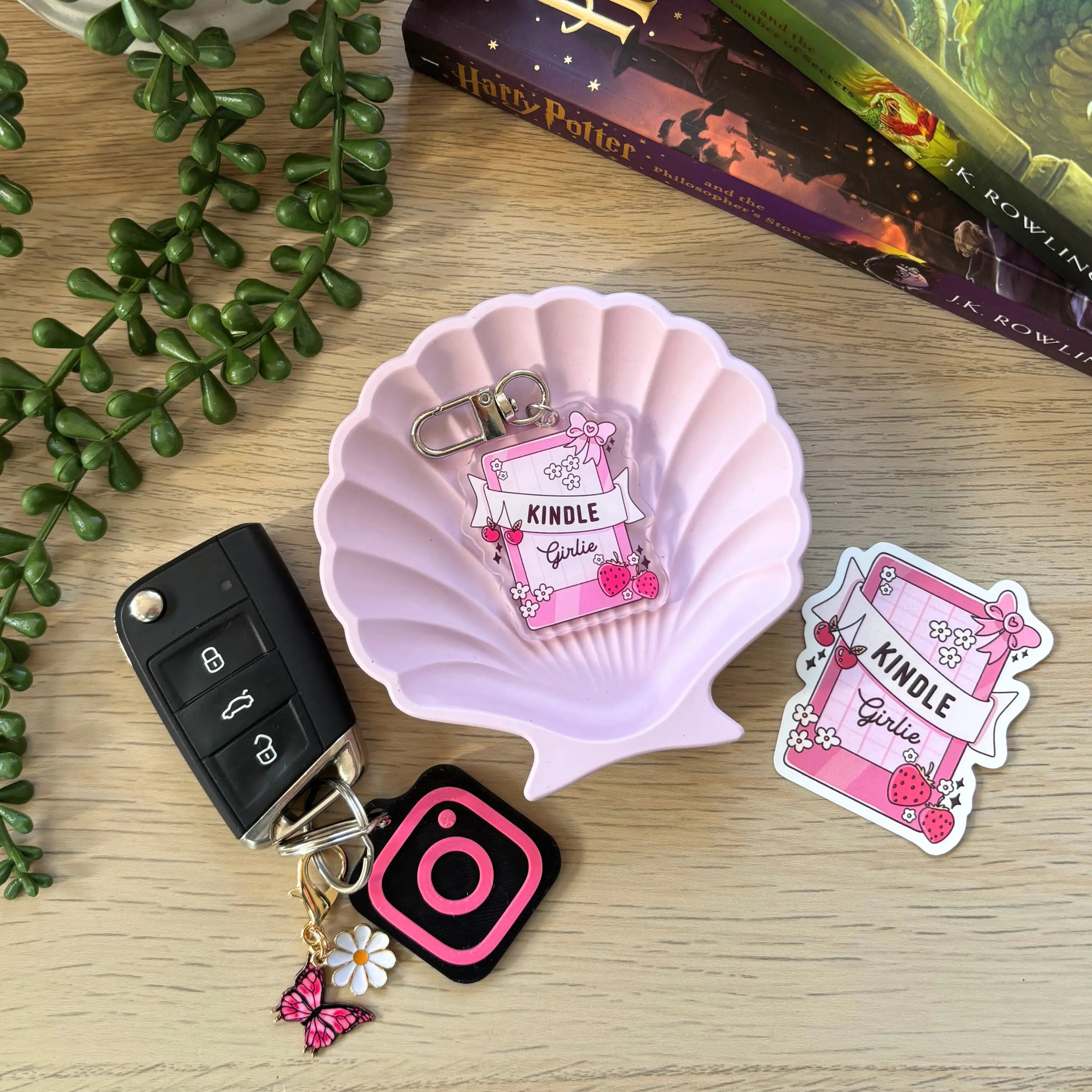 Pink Kindle-themed keyring with a small fairy charm and flower detail on a pink shell dish next to a black car key fob and.