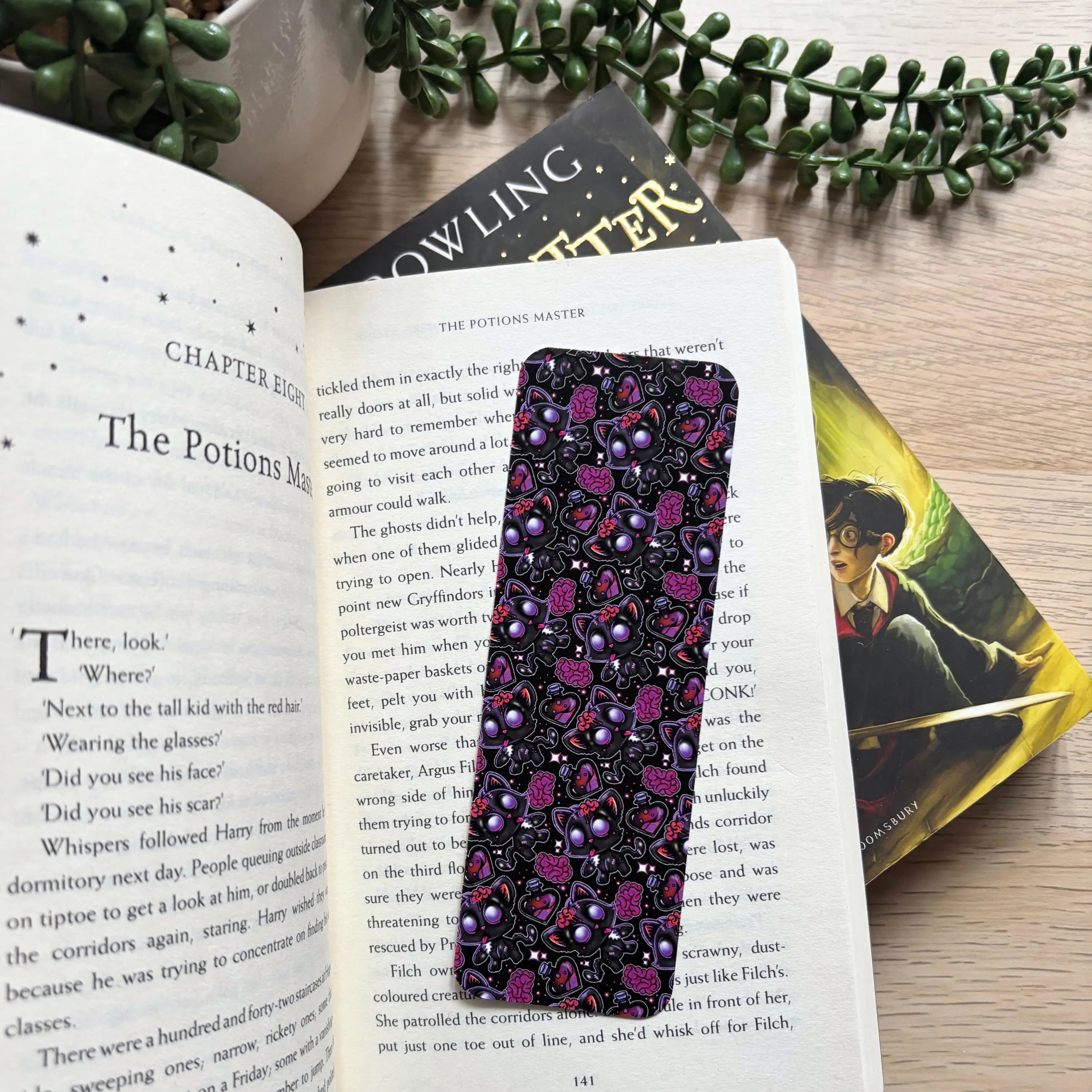 Black bookmark with colorful zombie kitty pattern in purple, pink, and white on an open book page.