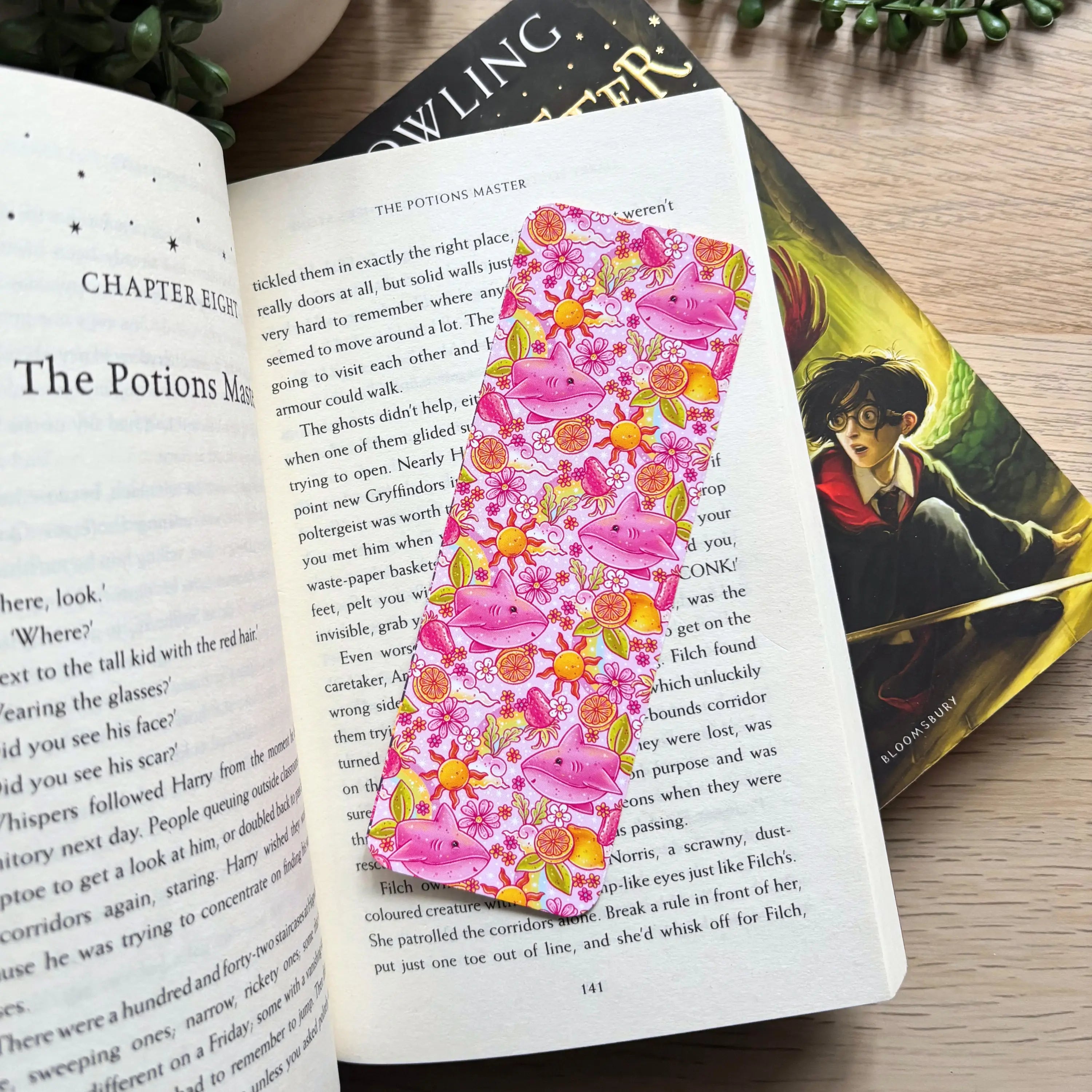 Pink floral bookmark with lemon shark illustration resting in open book pages.