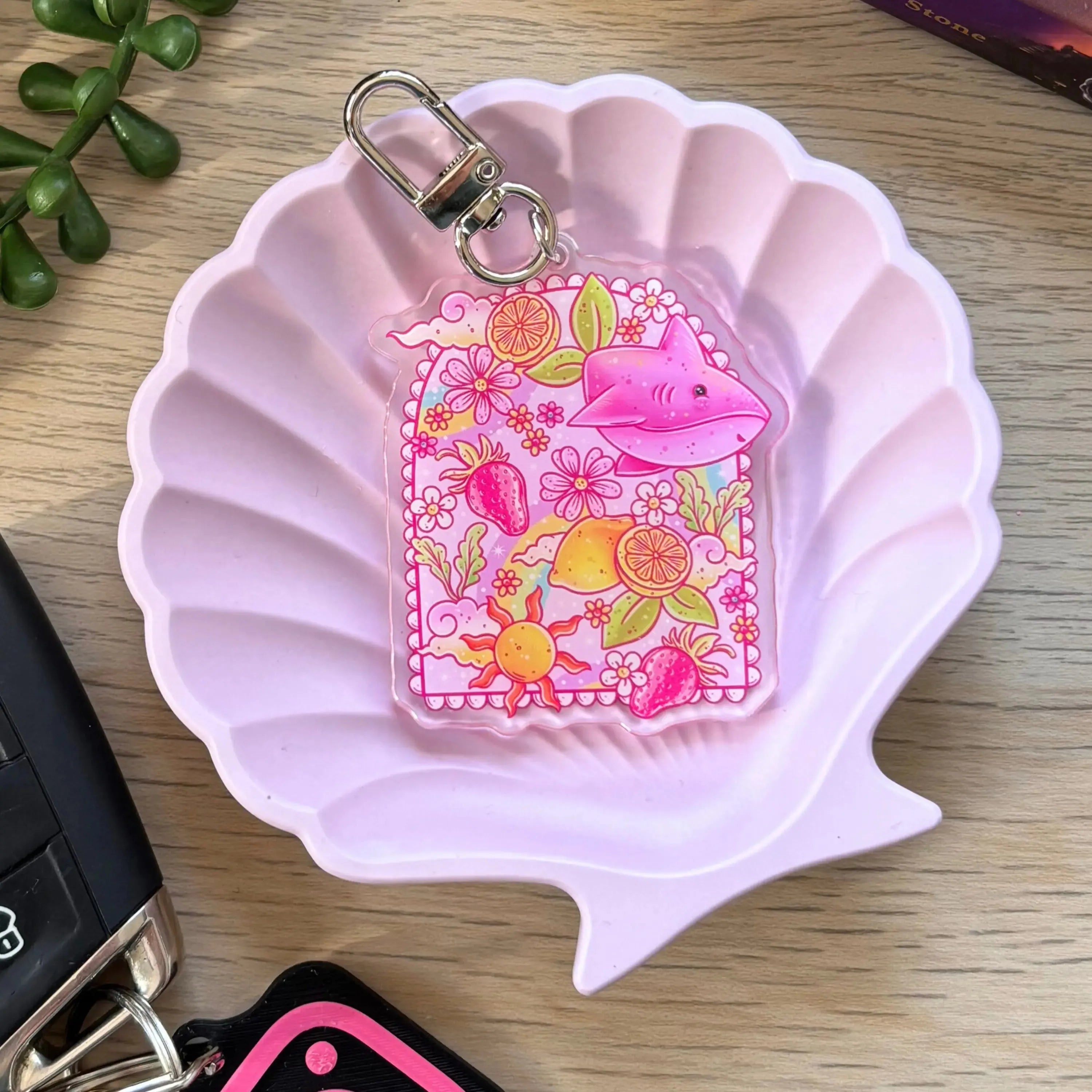 Clear acrylic keyring featuring a pink lemon shark surrounded by lemons and flowers on a pink scallop dish.