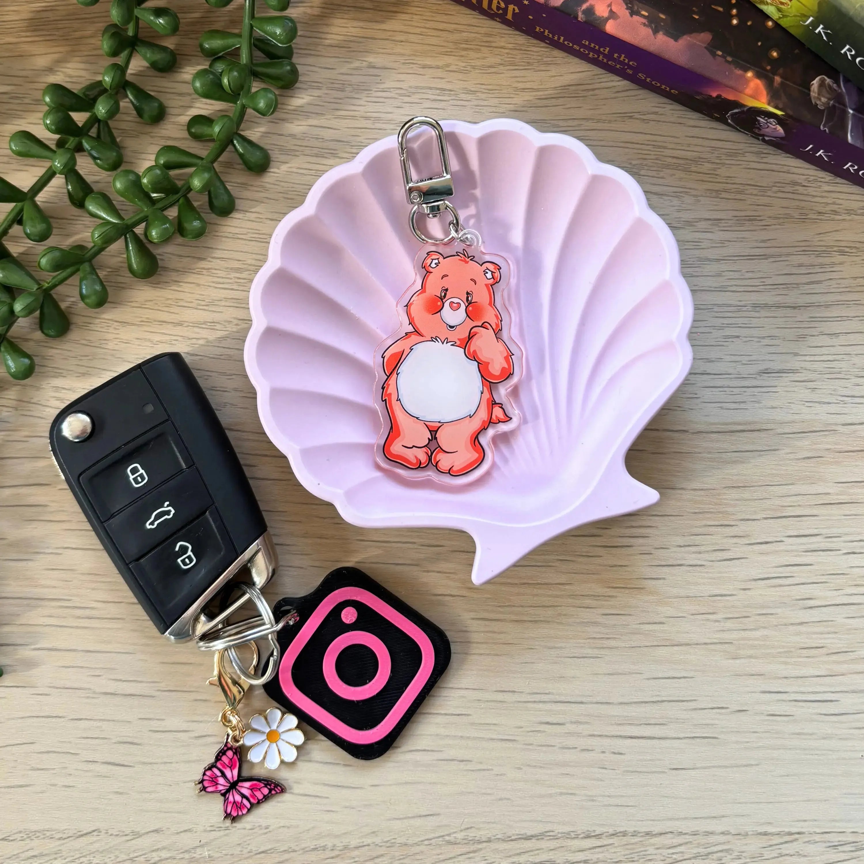 Orange colorful bear keyring with white belly and smiling face attached to a metal clip on a light pink shell-shaped dish.