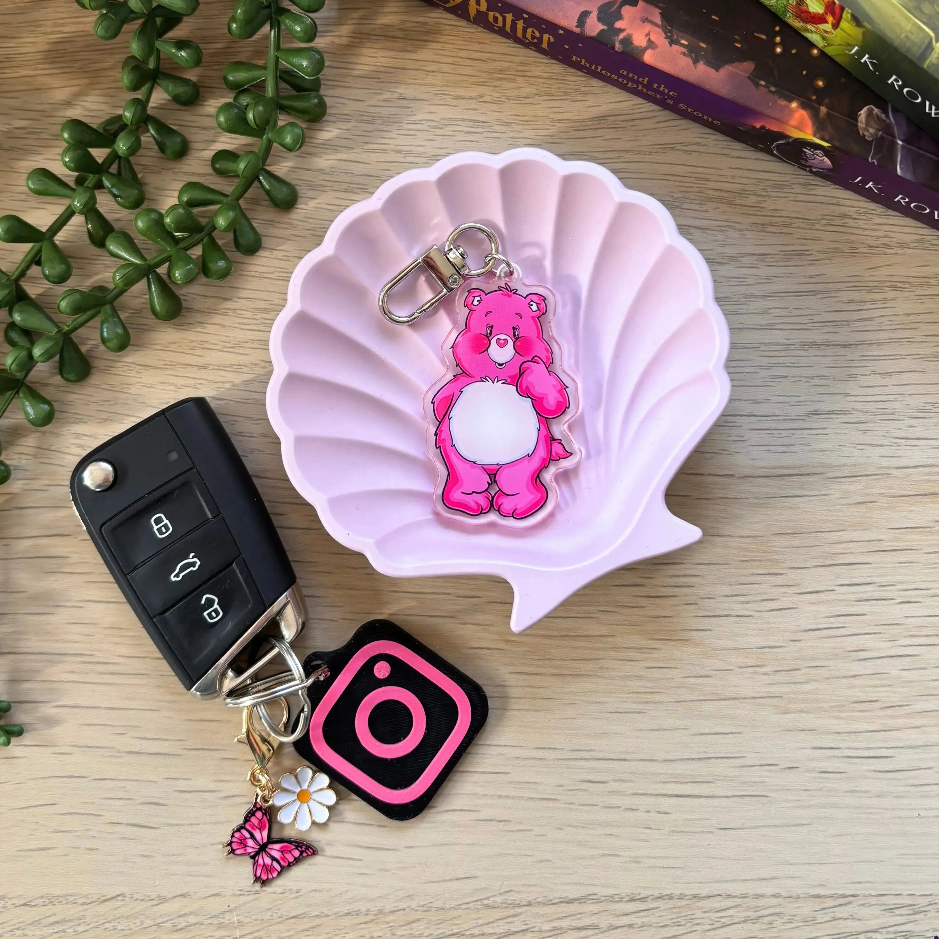 Pink colorful bear keyring with white belly attached to a metal clip, displayed on a pink shell-shaped dish.
