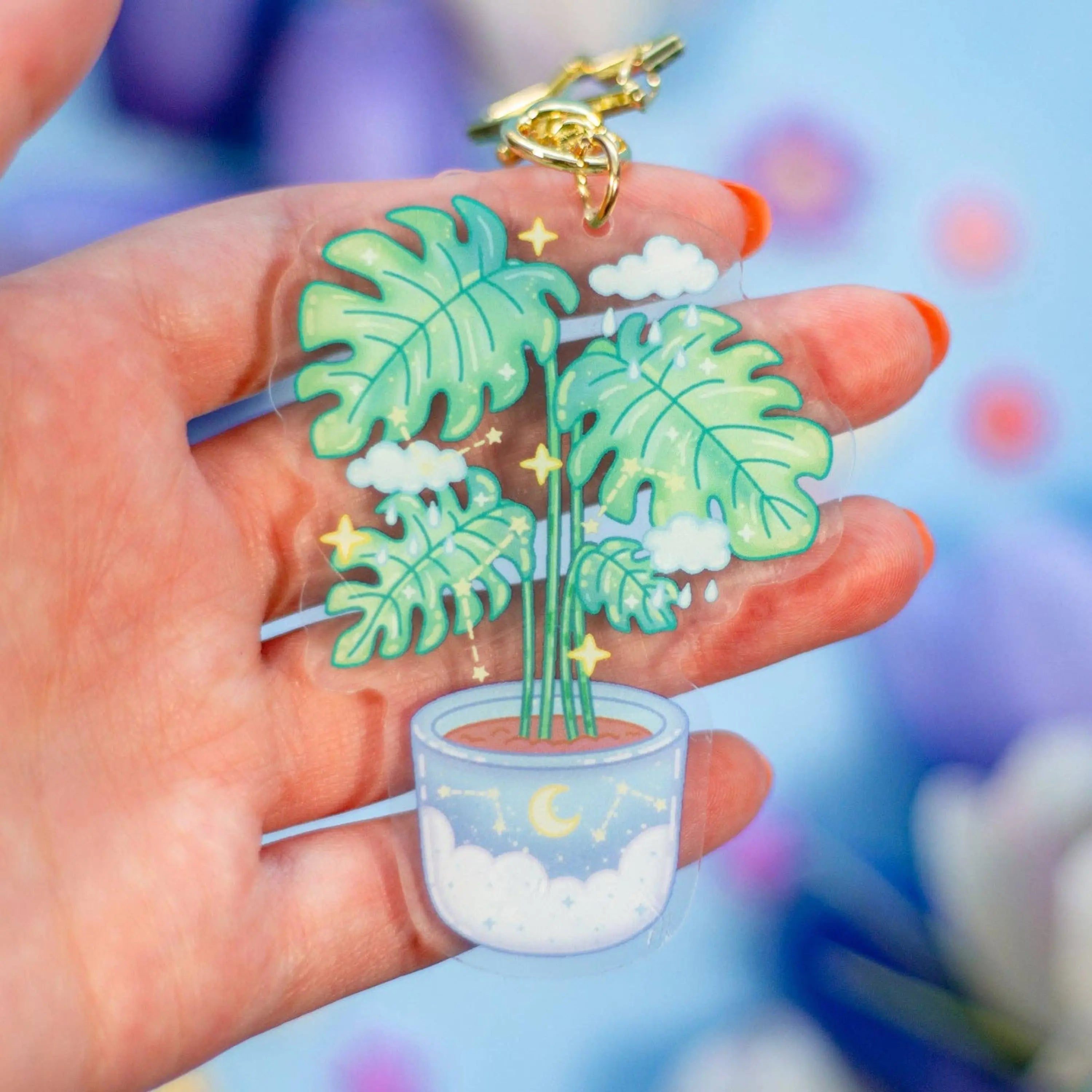 Keychain with potted plant design held in a hand against a colorful background