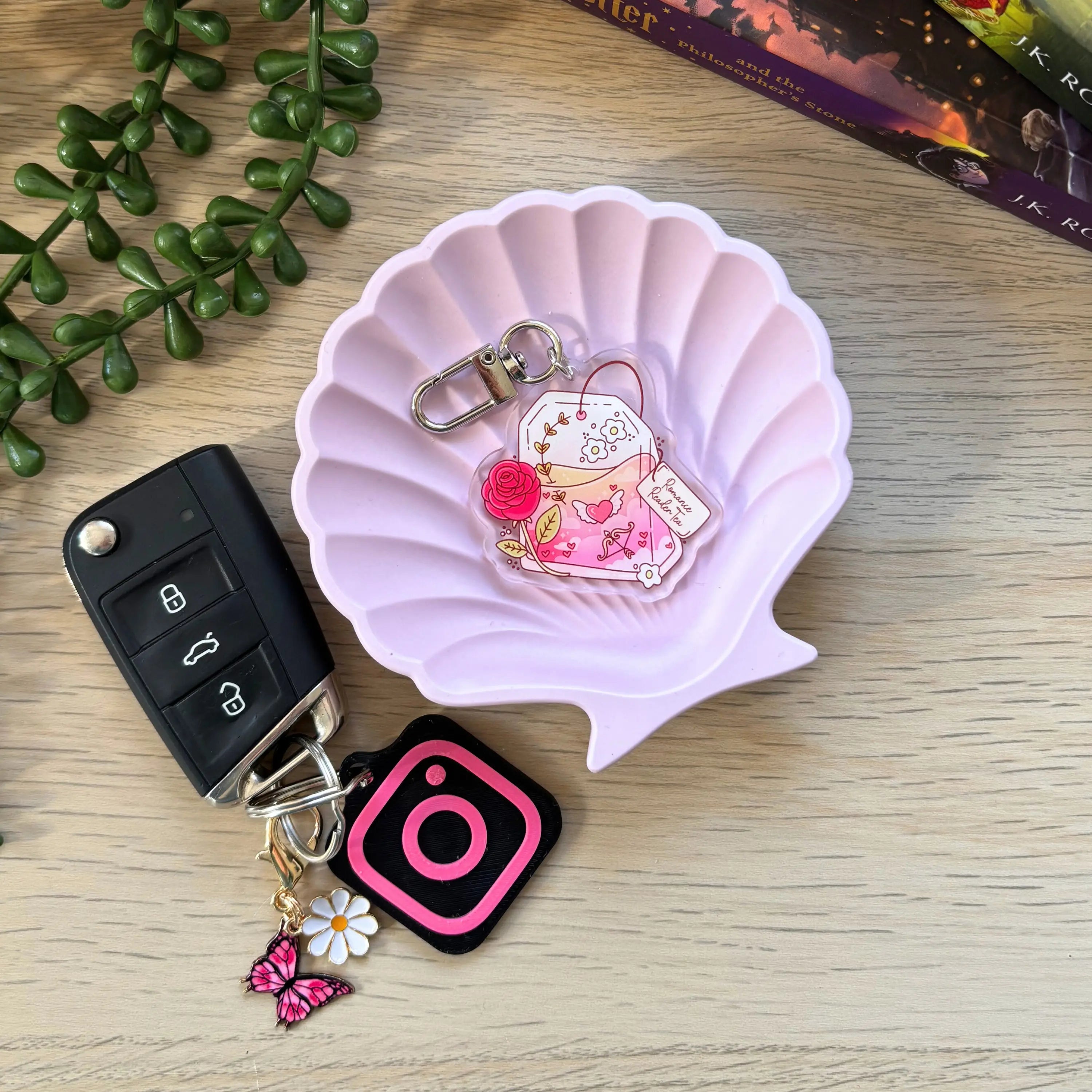Pink seashell tray holding a clear acrylic keyring with a cartoon girl reading surrounded by books and a rose charm.