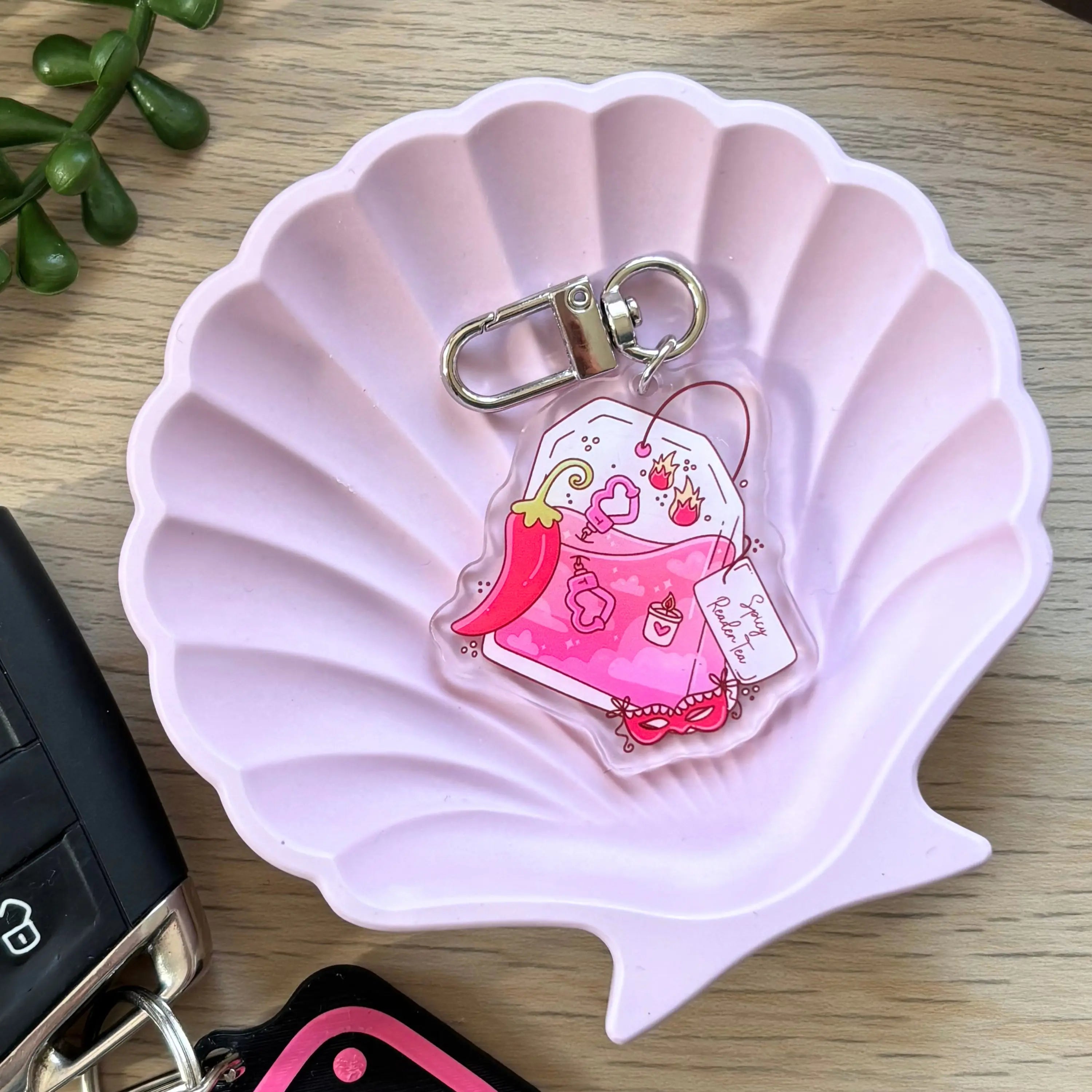 Cute pink chili pepper character keyring with smiling face and reading glasses on pink shell dish.