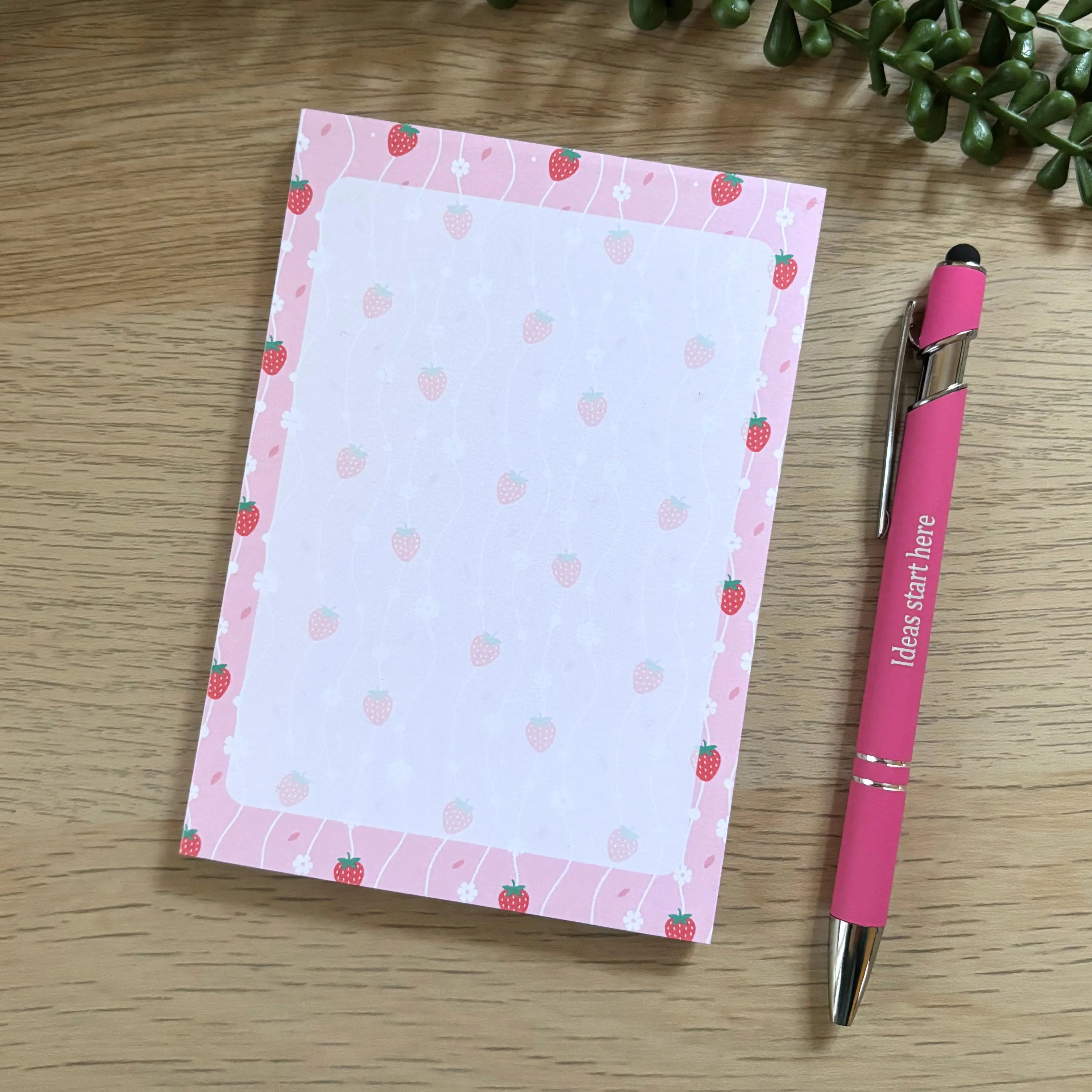 Small strawberry-themed notepad with pink border and scattered strawberry icons on white pages, next to pink pen.