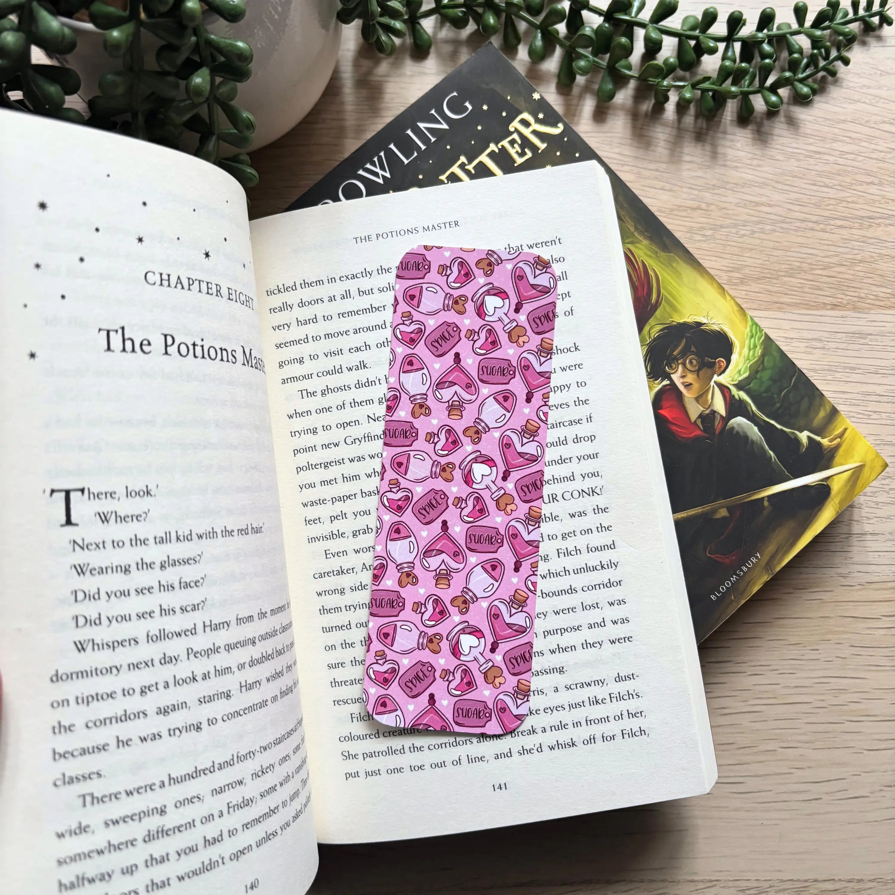 Pink rectangular bookmark with cute cartoon hearts and sweets pattern placed inside an open book.