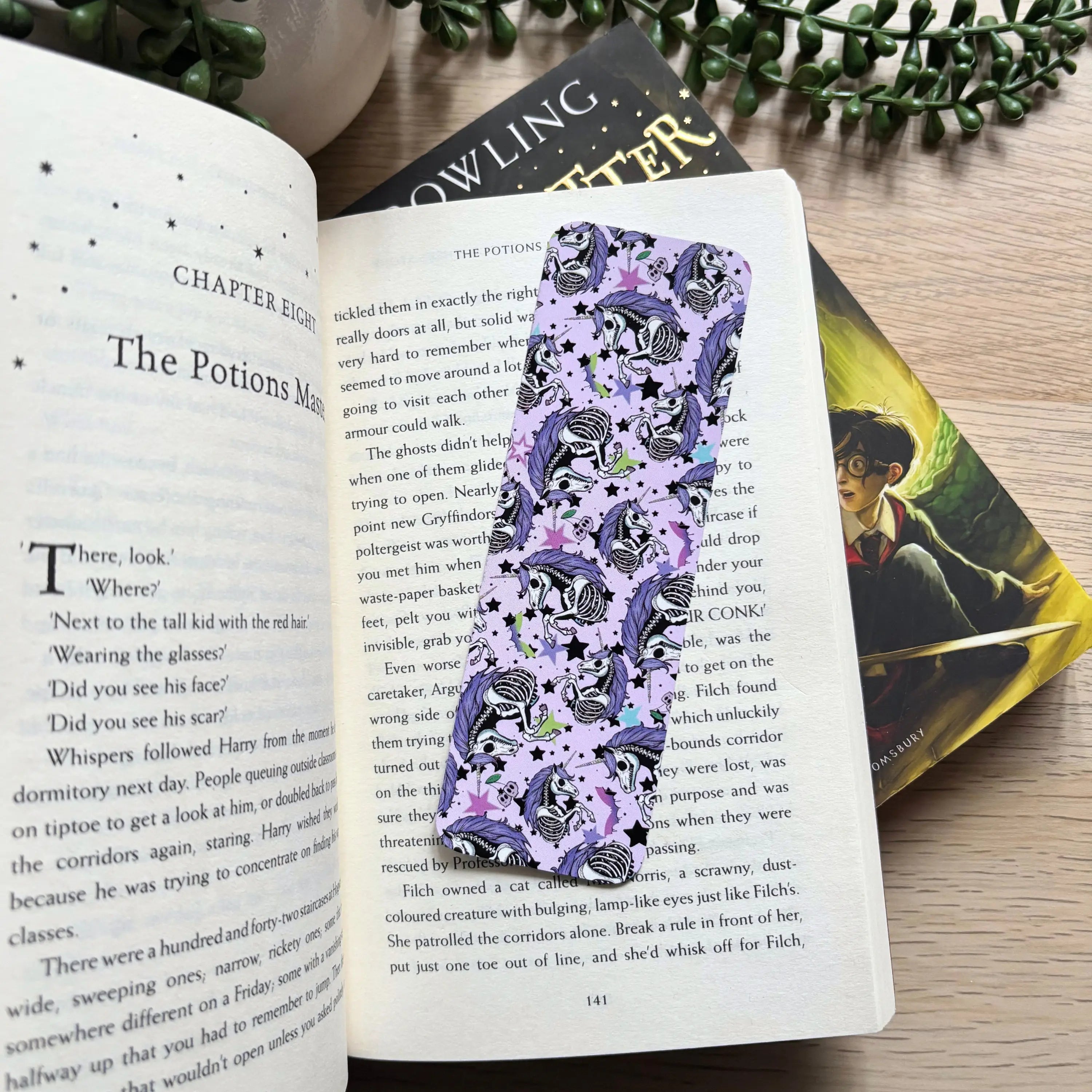 Purple skeleton unicorn bookmark with black stars and whimsical patterns on an open book page.
