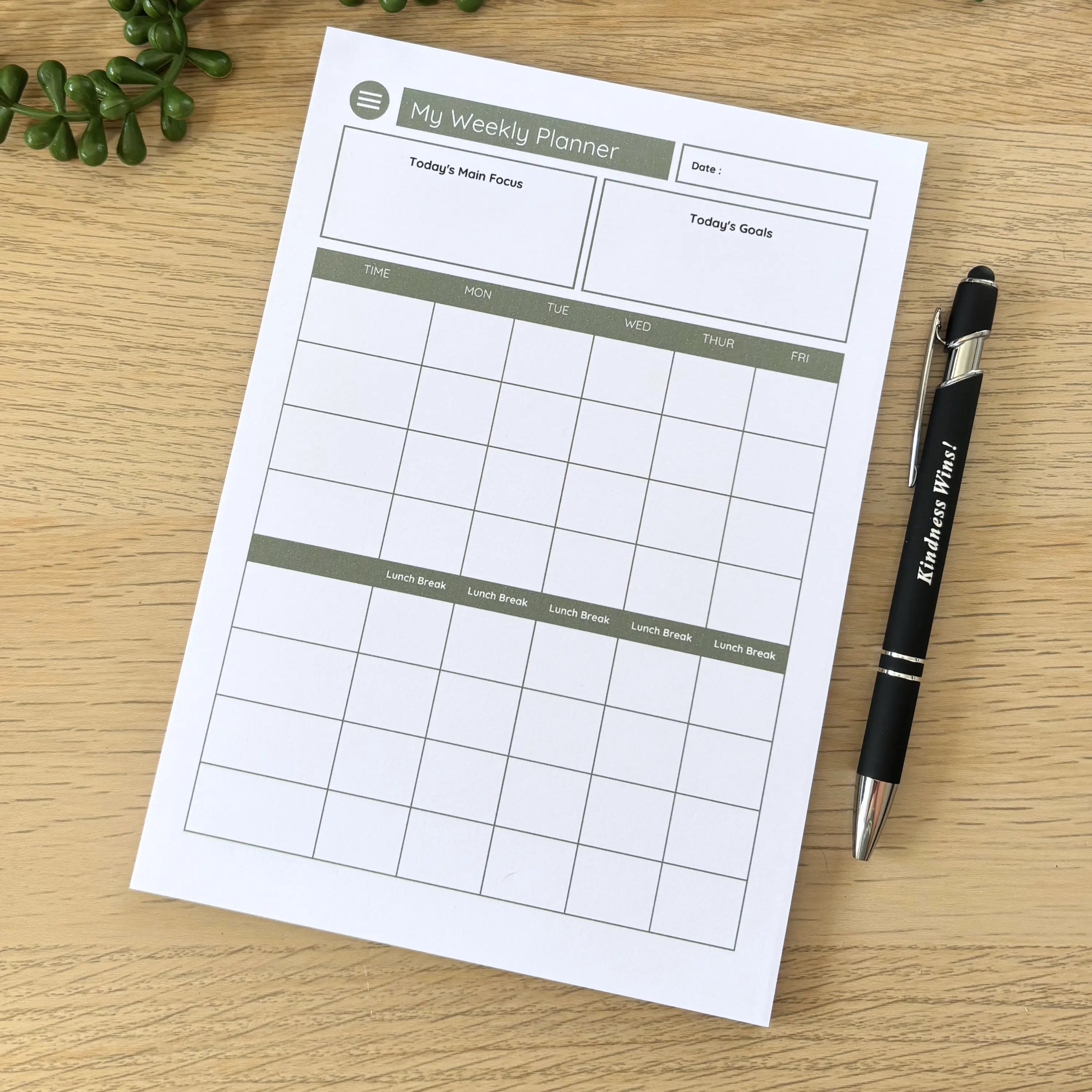 Minimalist weekly planner notepad with sage green headers and grid layout next to black pen on wooden surface.