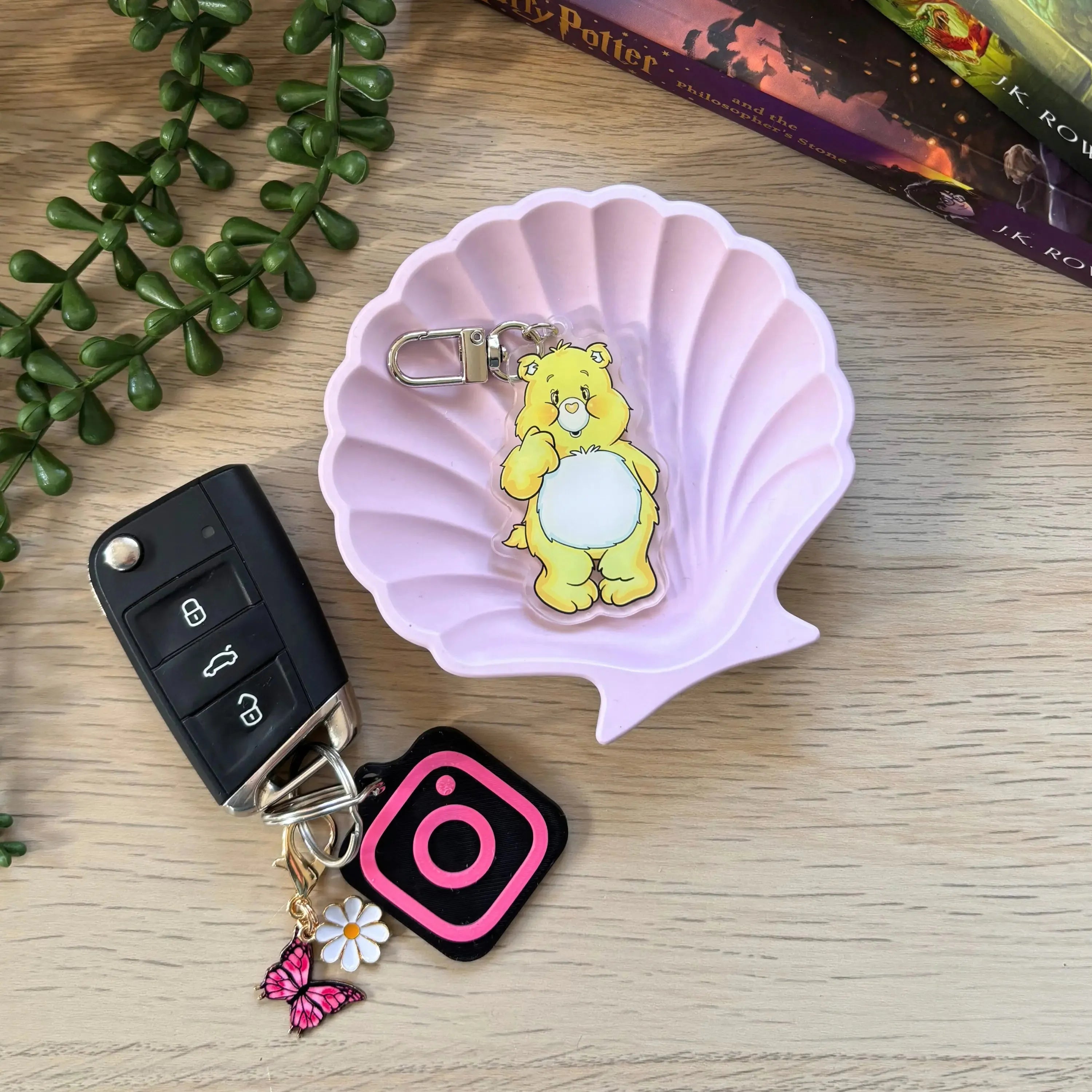 Yellow cartoon bear keyring with a white belly and clasp attachment on a pink shell dish.
