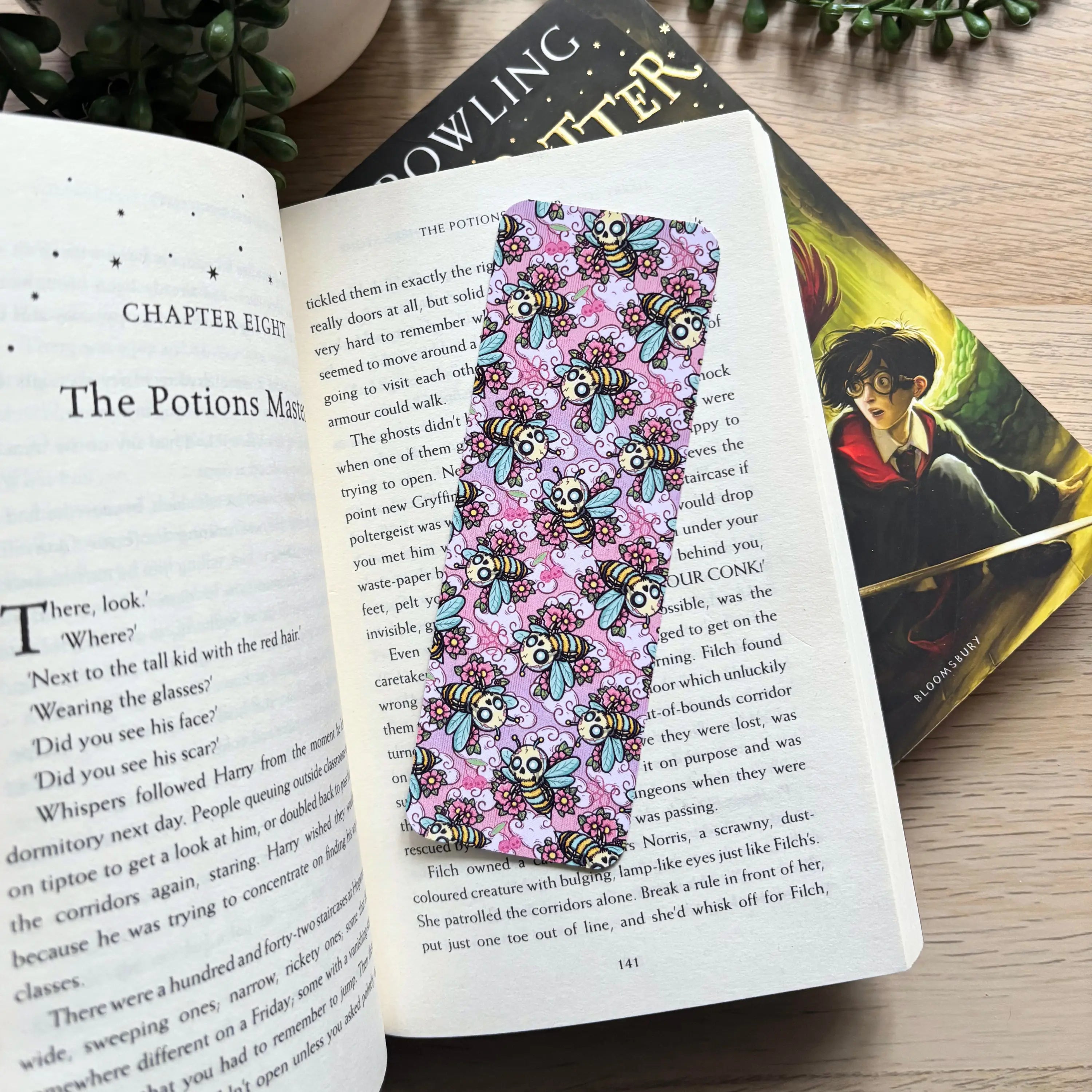 Colorful bookmark with cute spooky zombie bees on a pink background, inserted in an open book.